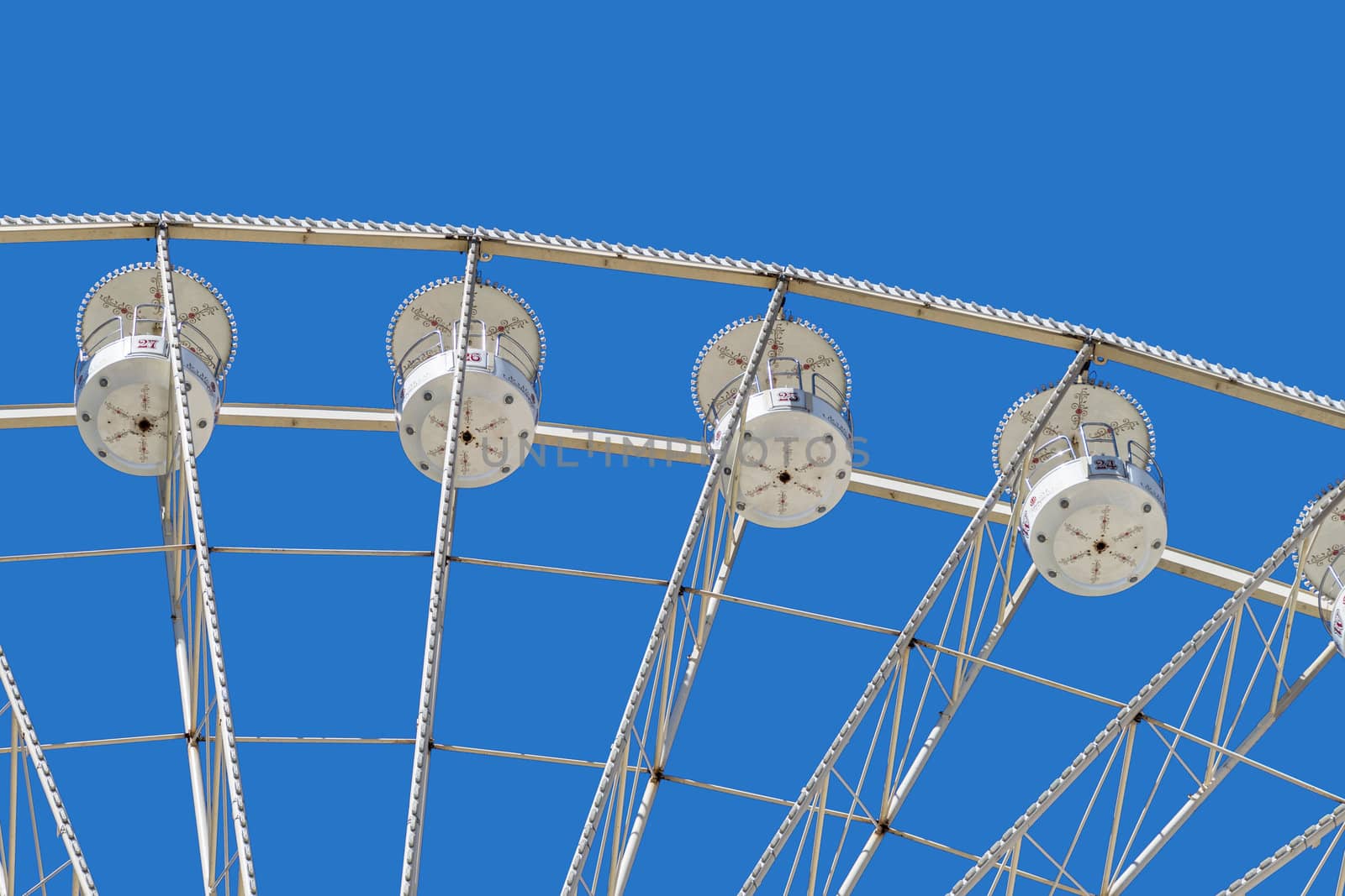 Ferris wheel with white cabins for the passengers, seen from below, at a fairground