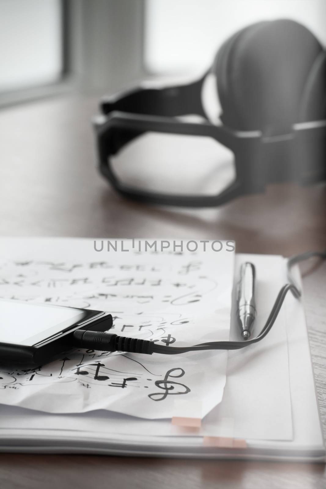 Closeup of smartphone with headphone on musical notes paper on wooden desk 