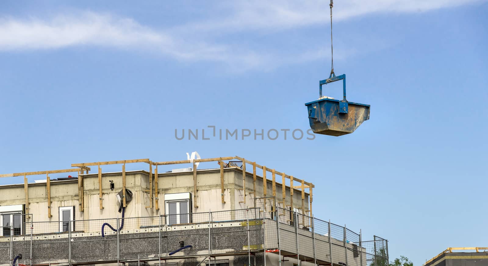 A blue container with building materials floats above the construction site with the shell of a large office building, germany