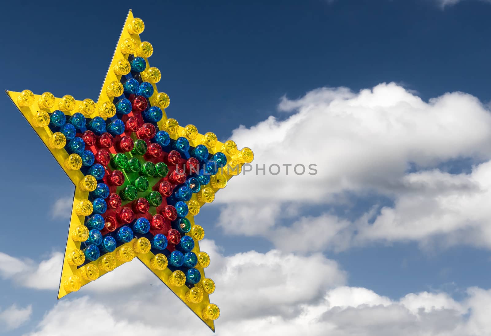 Large colorful star of differently colored lamps exempted in front of a blue sky with clouds, illustration