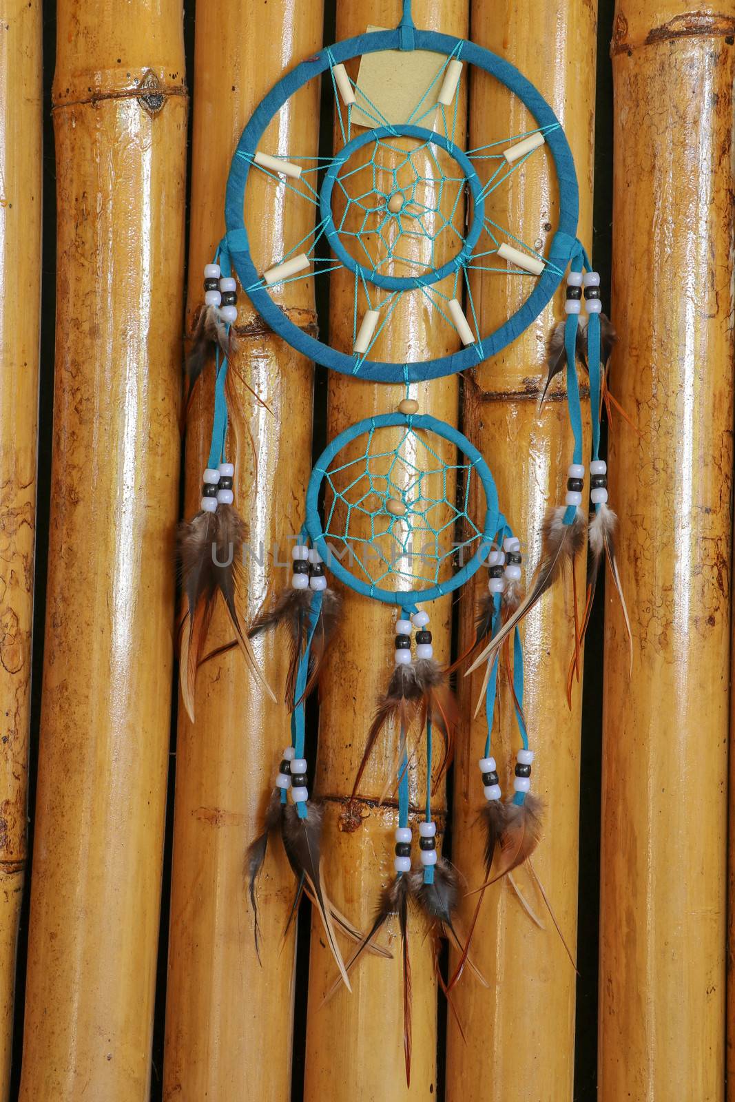 Blue Dreamcatcher with feathers and beads isolated on a bamboo background.