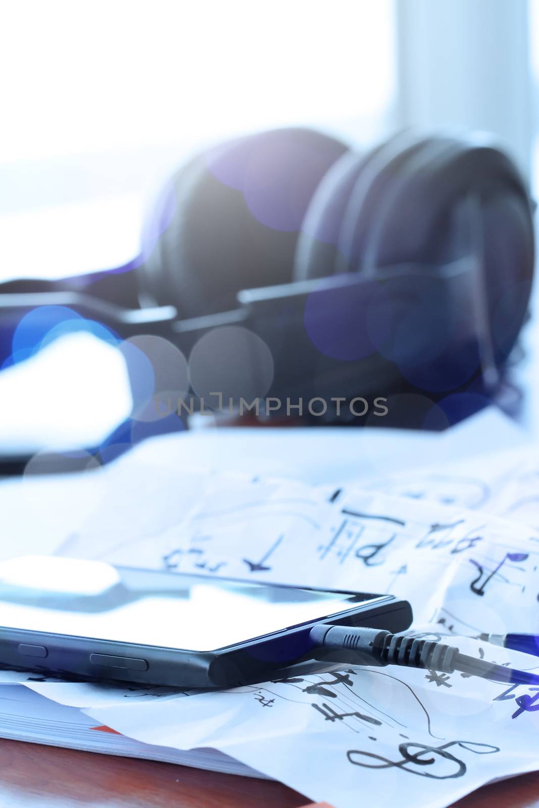 Closeup of smart phone with headphone on musical notes paper with shallow DOF evenly matched on wooden desk