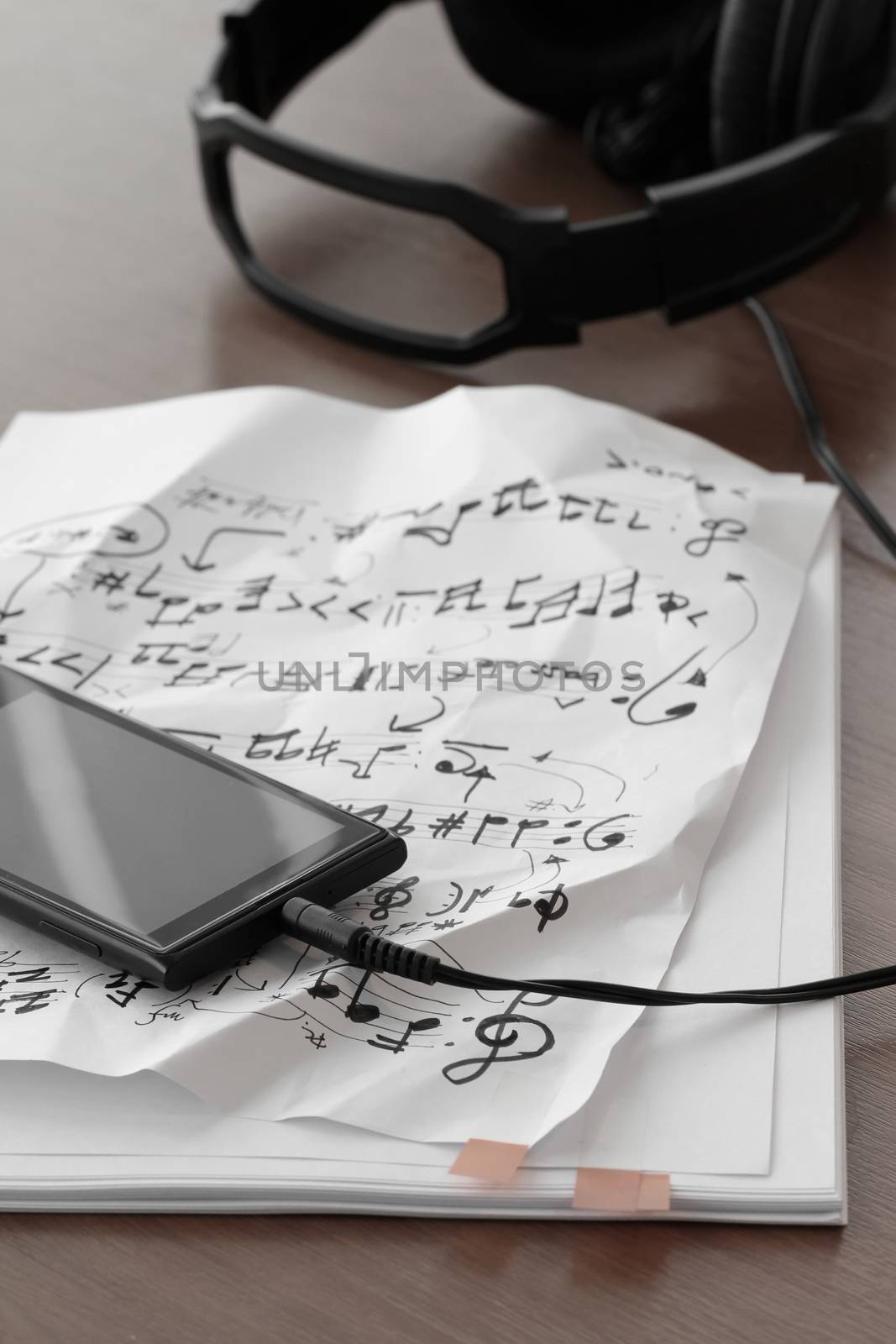 Closeup of smartphone with headphone on musical notes paper on wooden desk 