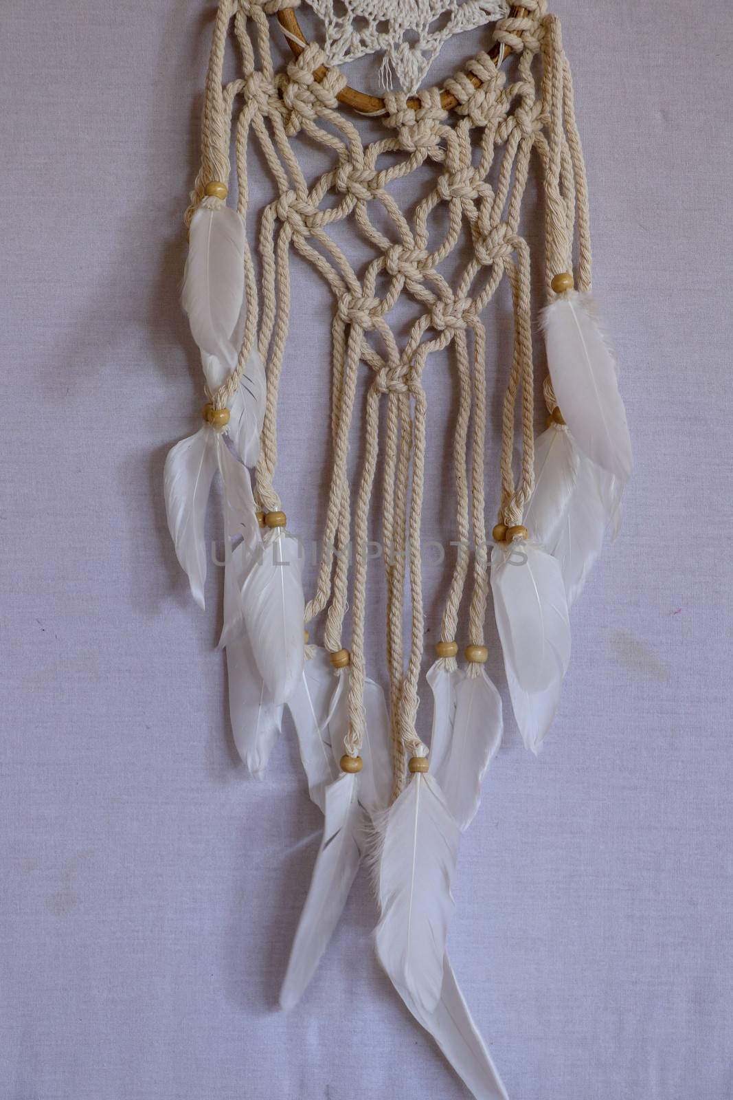 Handmade pink dream catcher with white doily on background of rocks and lake. Tribal elements, feathers, lace, crochet snowflake.