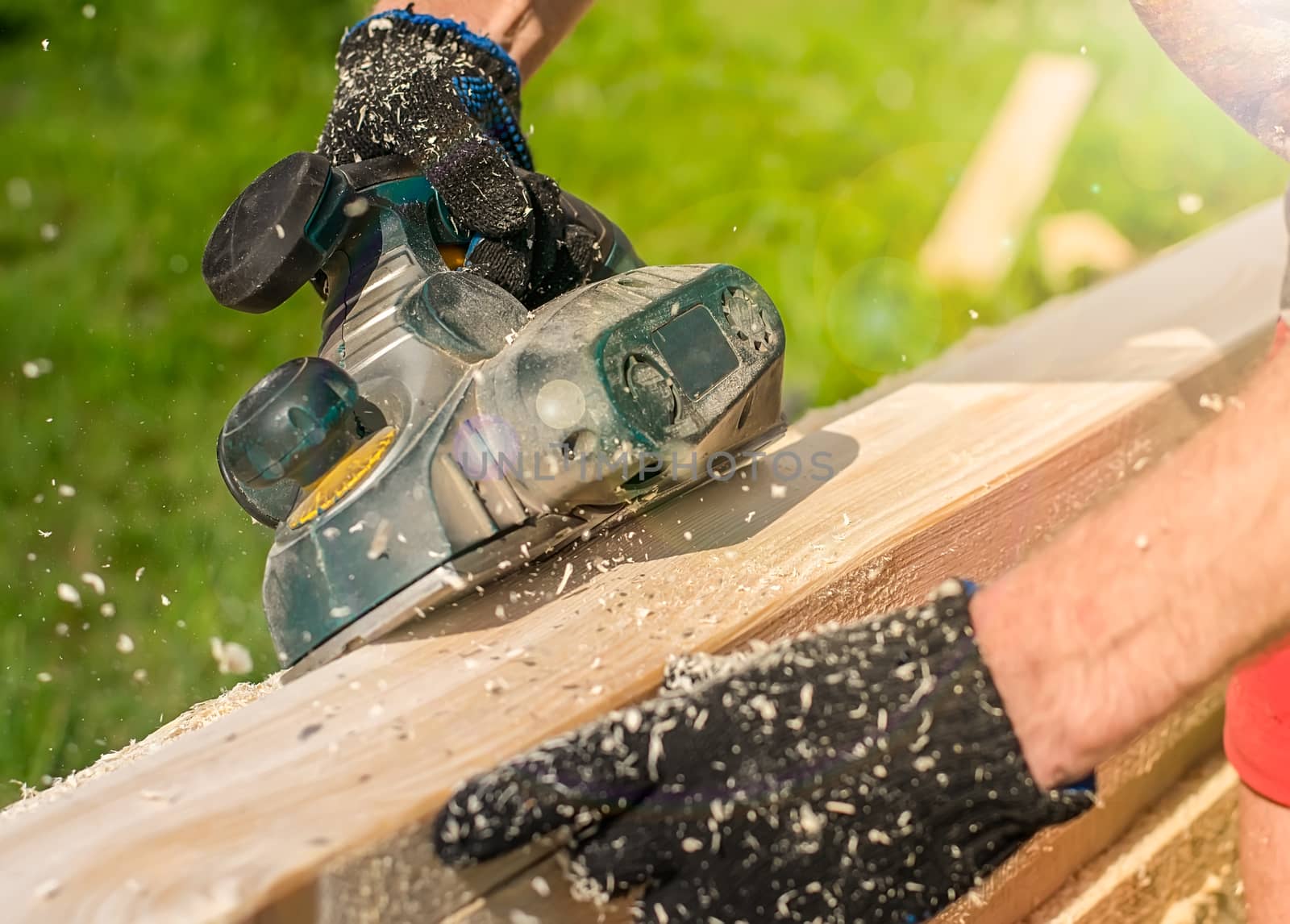 carpenter hands in gloves with an electric tool, plane, process wooden boards, lumber