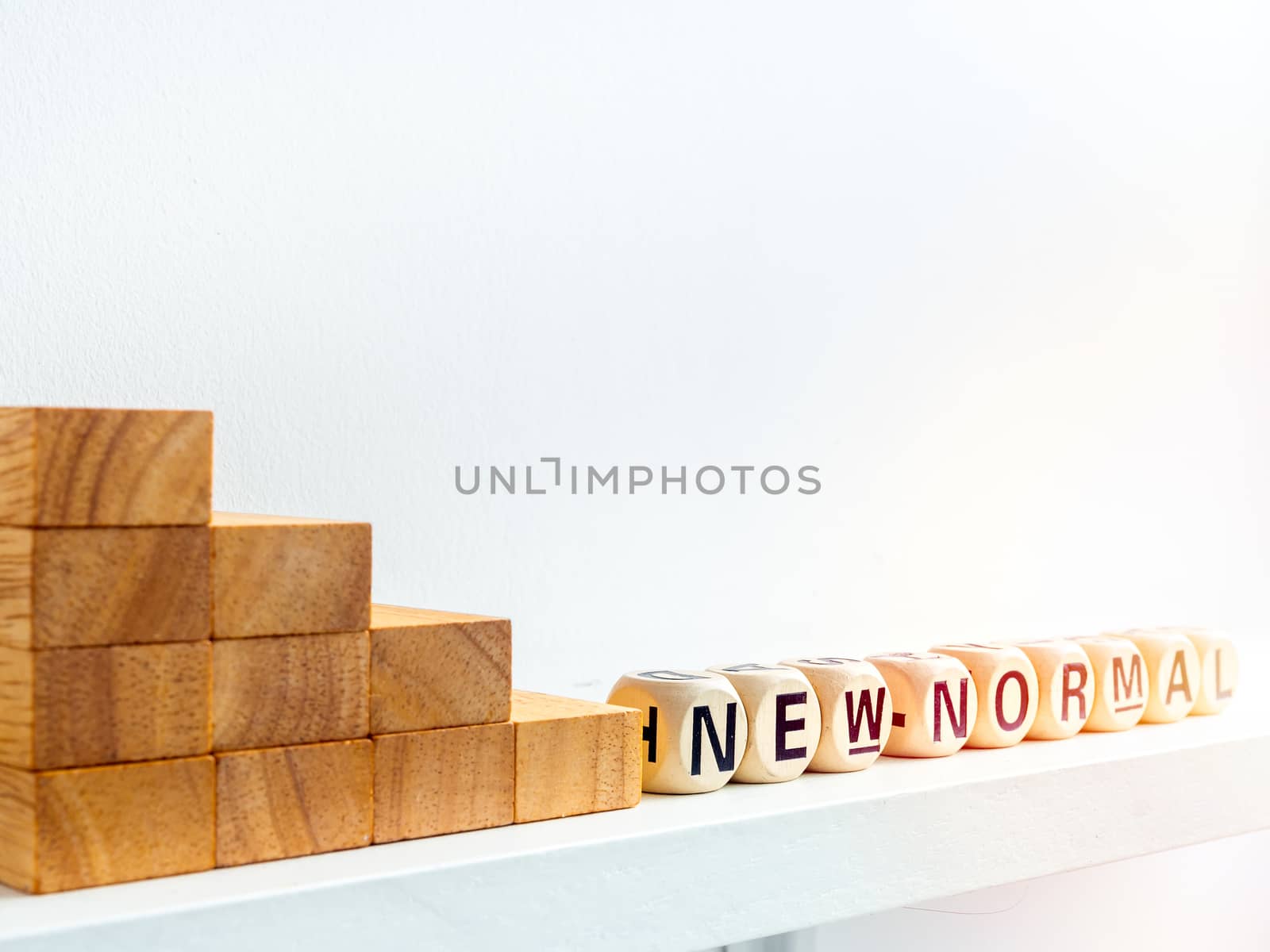 Stairs down to New Normal, words on wooden alphabet cube on white background with sunlight. New normal after covid-19 pandemic concept.