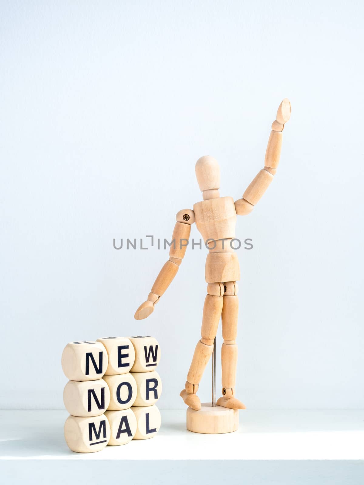 New Normal, words on wooden alphabet cube and wooden figure raising up hand on white background, vertical style. New normal life after covid-19 pandemic concept.