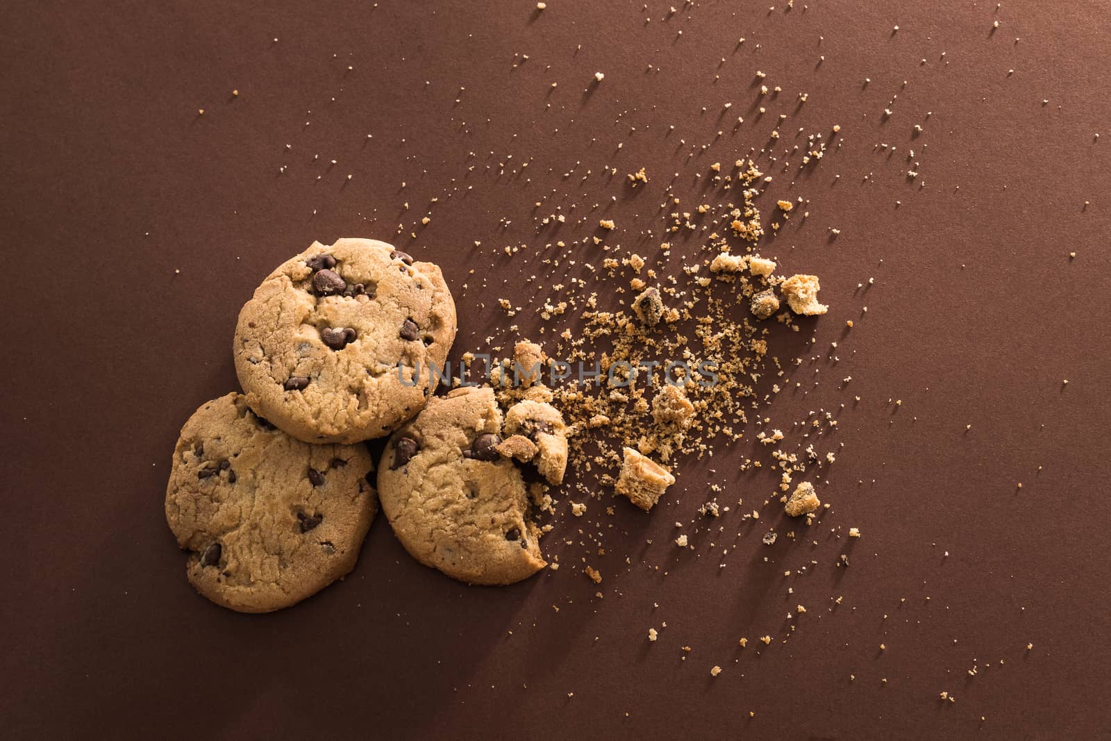 Broken chocolate chip cookies on brown background. Top view. Copy space.