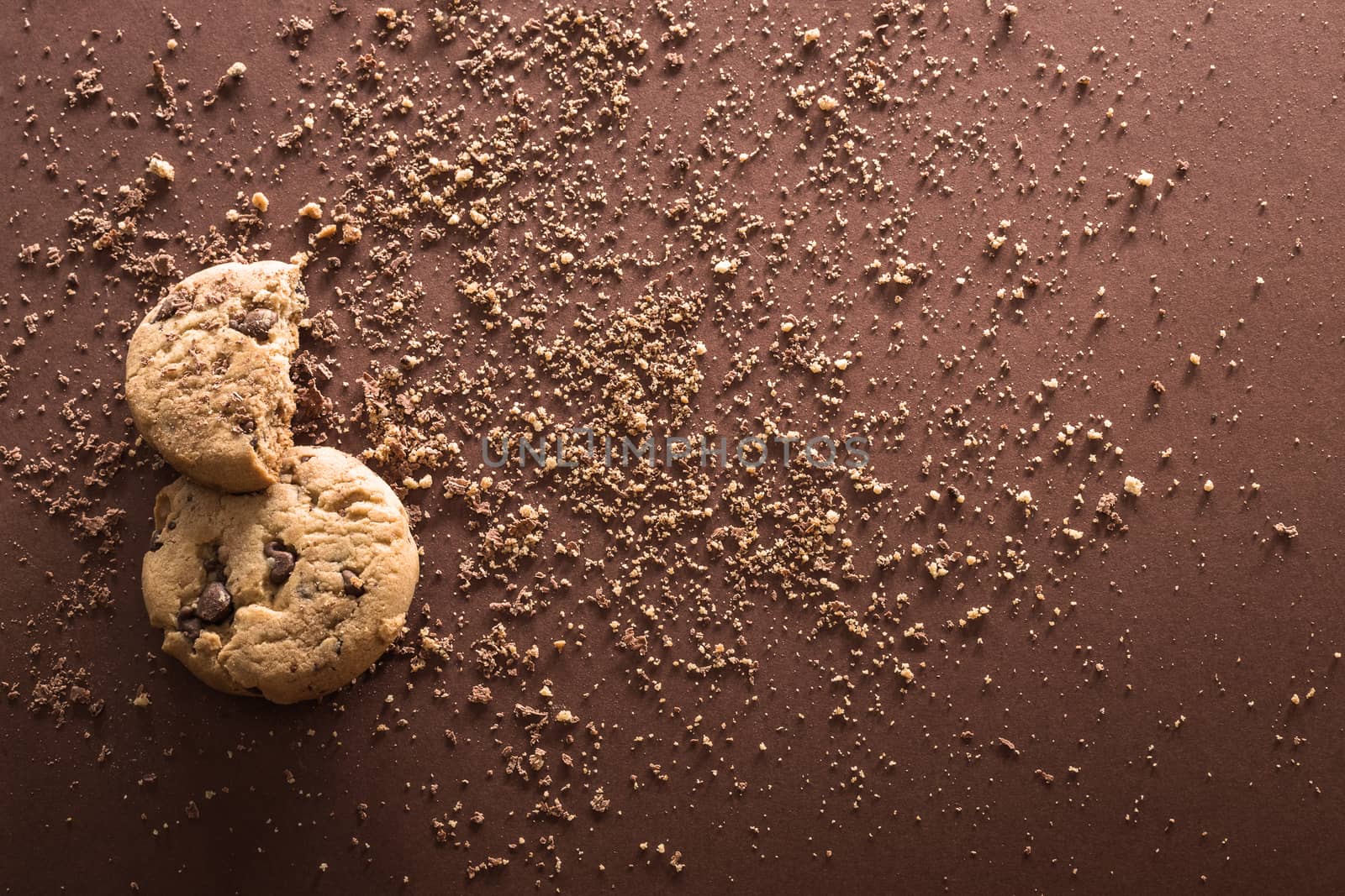 Broken chocolate chip cookies on brown background. Top view. Copy space.