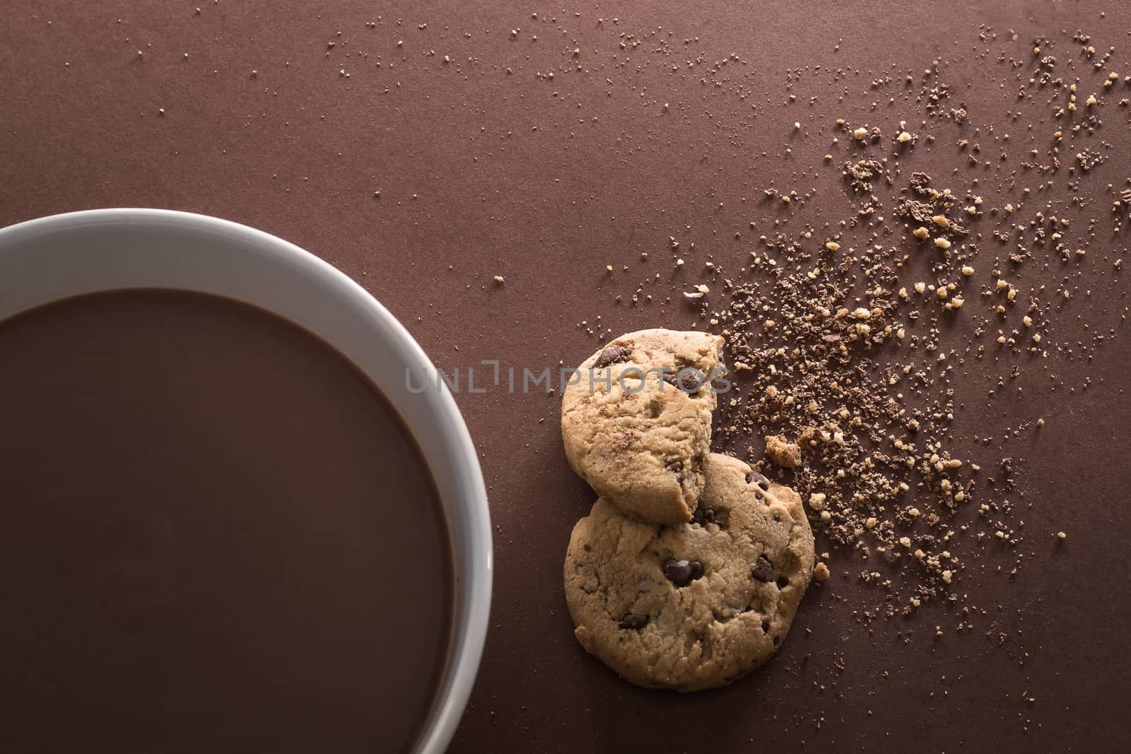 Chocolate white bowl and broken chocolate chip cookies on brown background. Top view. Copy space.