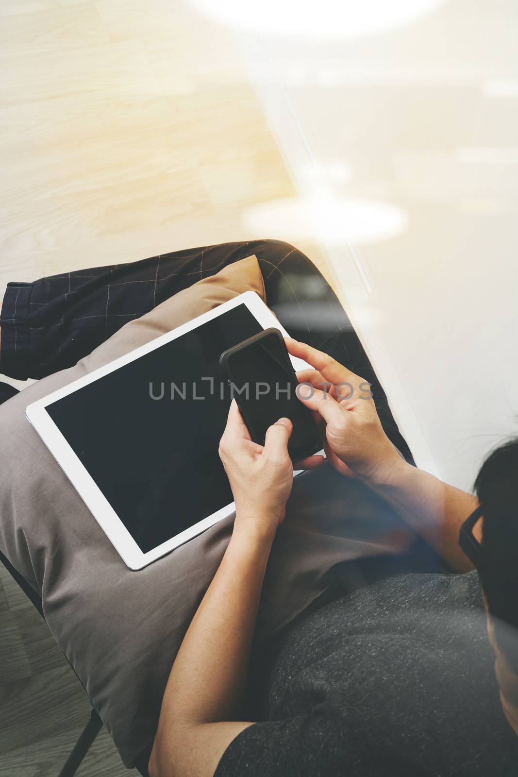 top view of hipster hands using smart phone and digital tablet pro while sitting on a cosy sofa in his home as concept