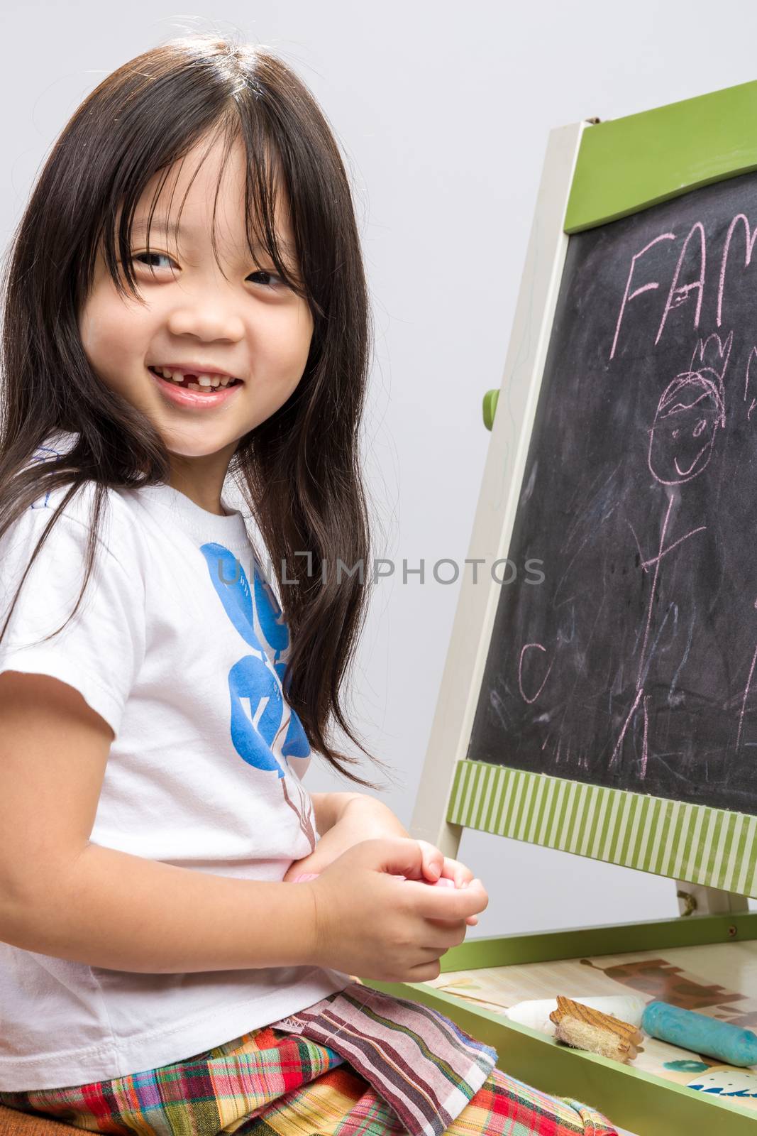 Little kid sit beside a blackboard studio isolated.