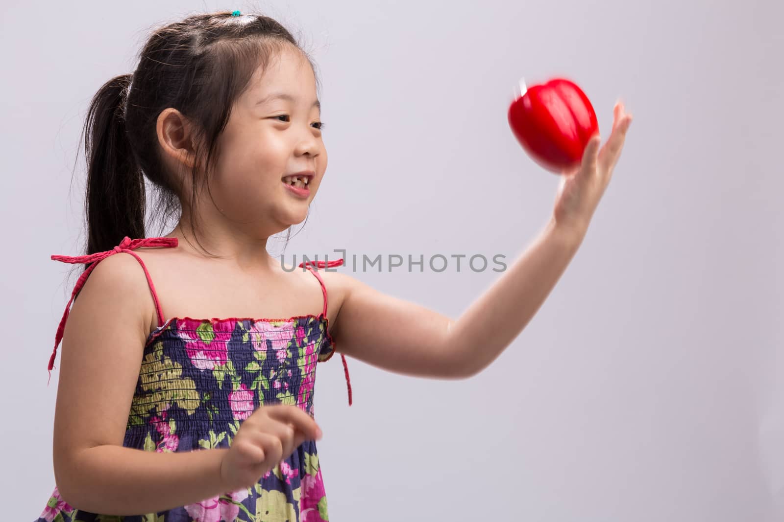 Little girl is throwing a red bell pepper in the air.