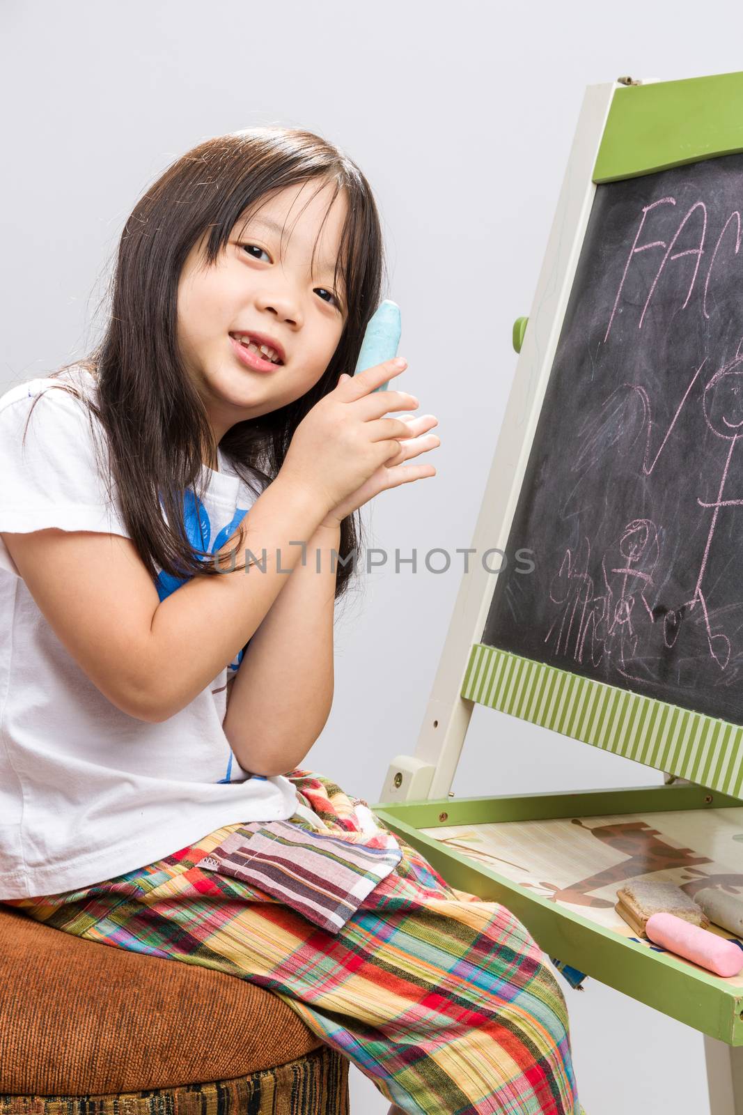 Little kid sit beside a blackboard studio isolated.