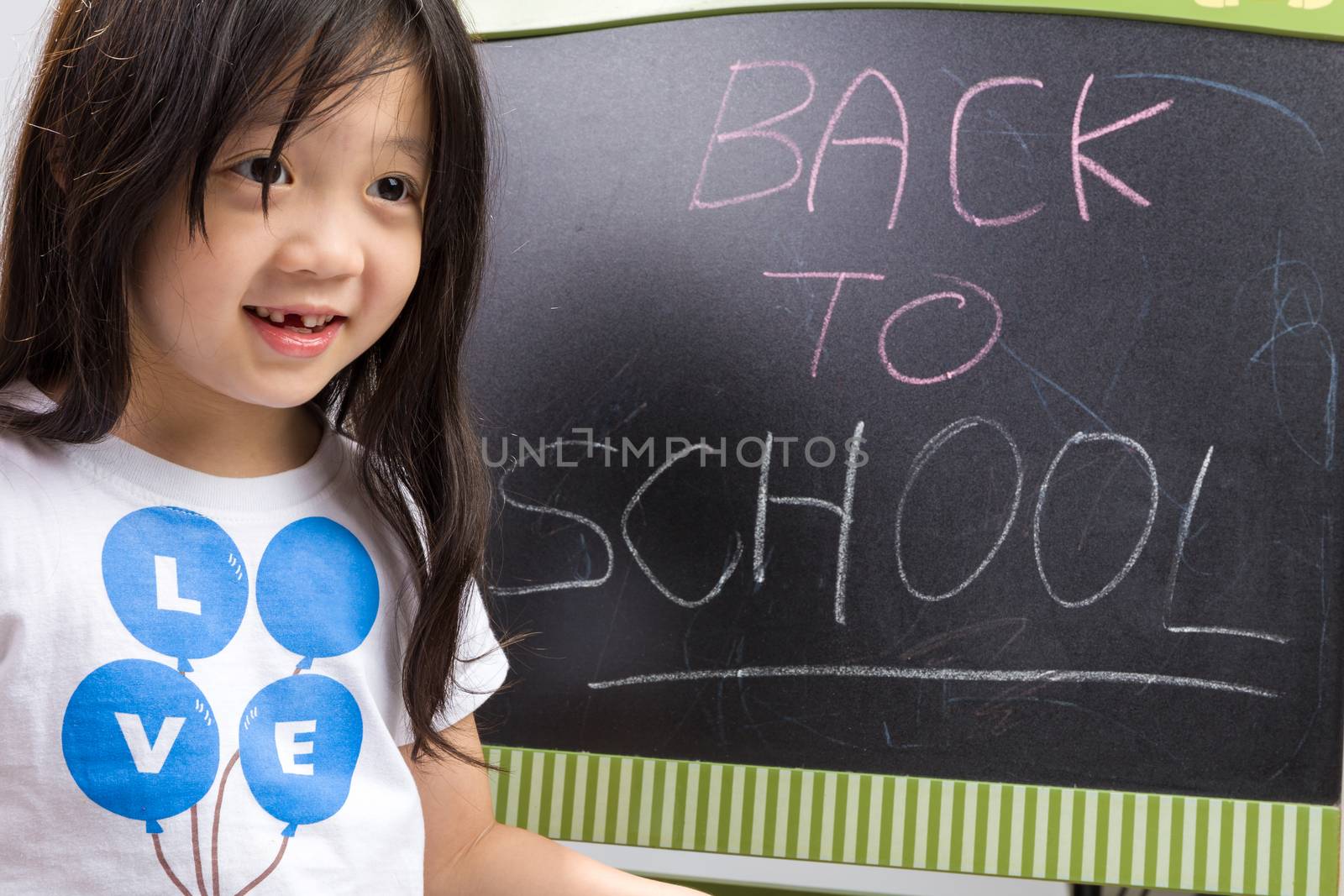 Child holding book in her hands beside blackboard to illustrate education concept.