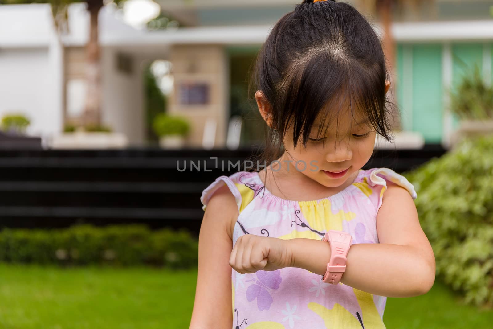 Child standing in garden using smartwatch or smart watch on her wrist.