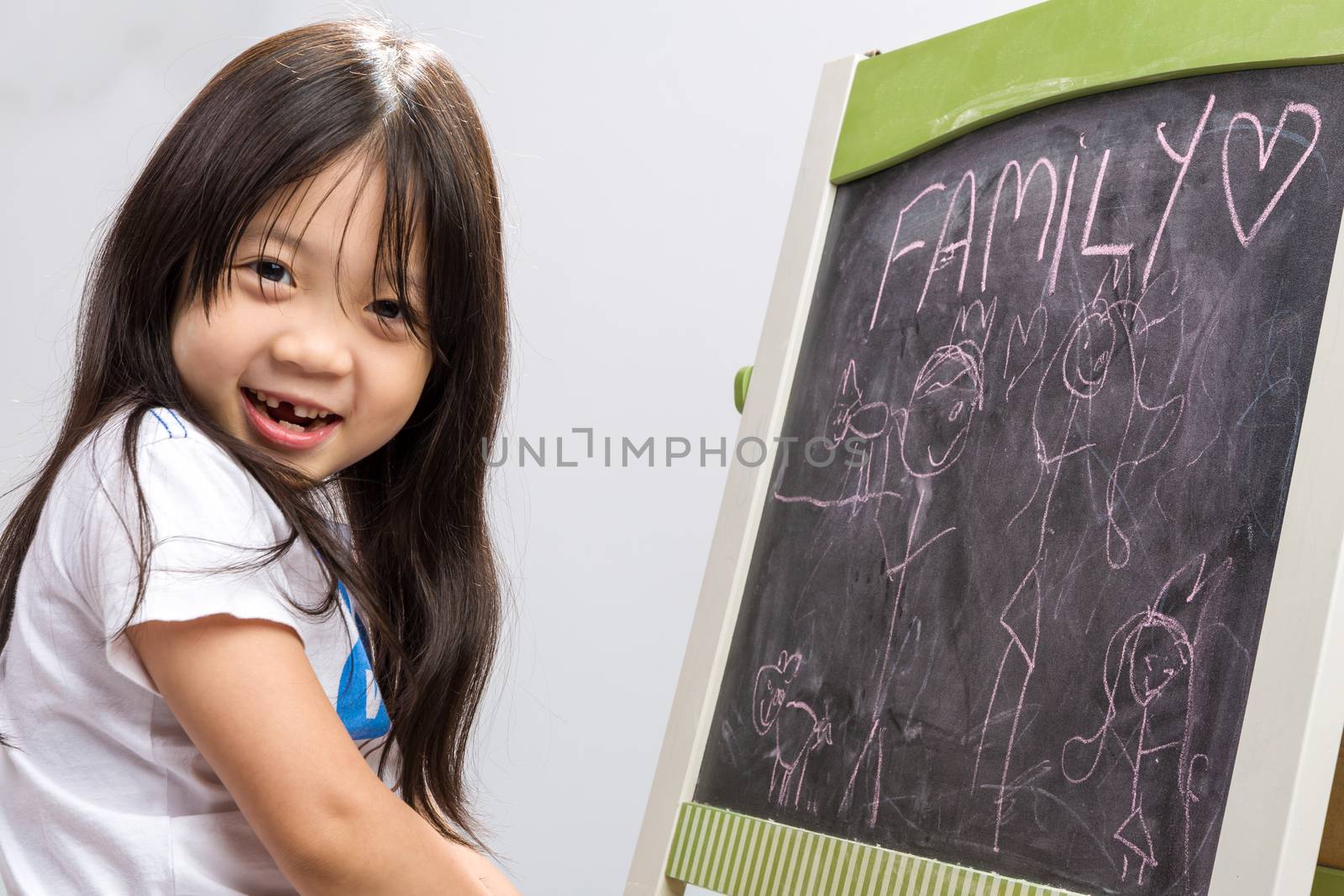 Little kid sit beside a blackboard studio isolated.