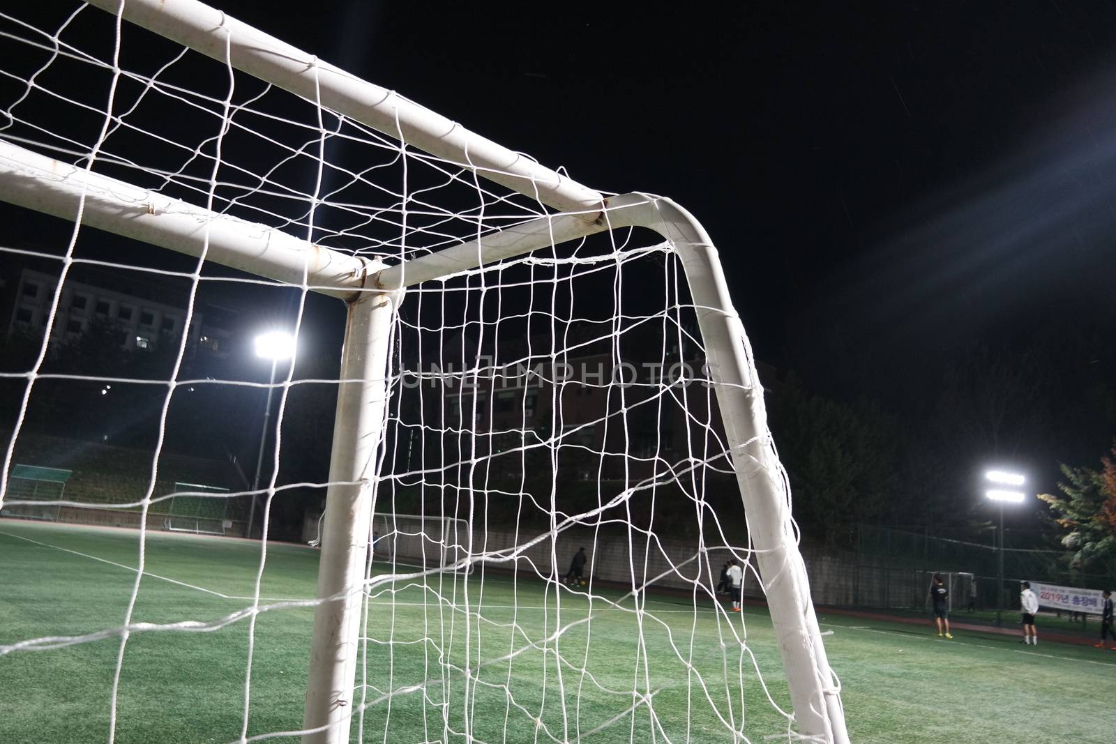 Night view of a soccer goal net under flood lights. Closeup view of goal net in a soccer playground