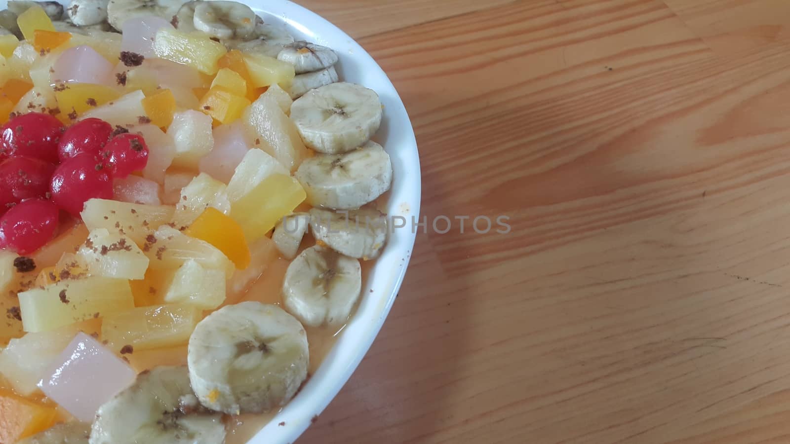 Creamy tasty sweet fruit trifle over custard with banana slices layered on surface on wooden floor. A top view of home made fruit trifle, a products for dessert after meal.