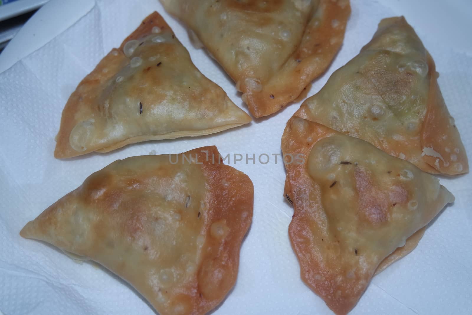 Closeup of delicious home made spicy and crunchy samosa pastries placed in a white ceramic plate on wooden floor