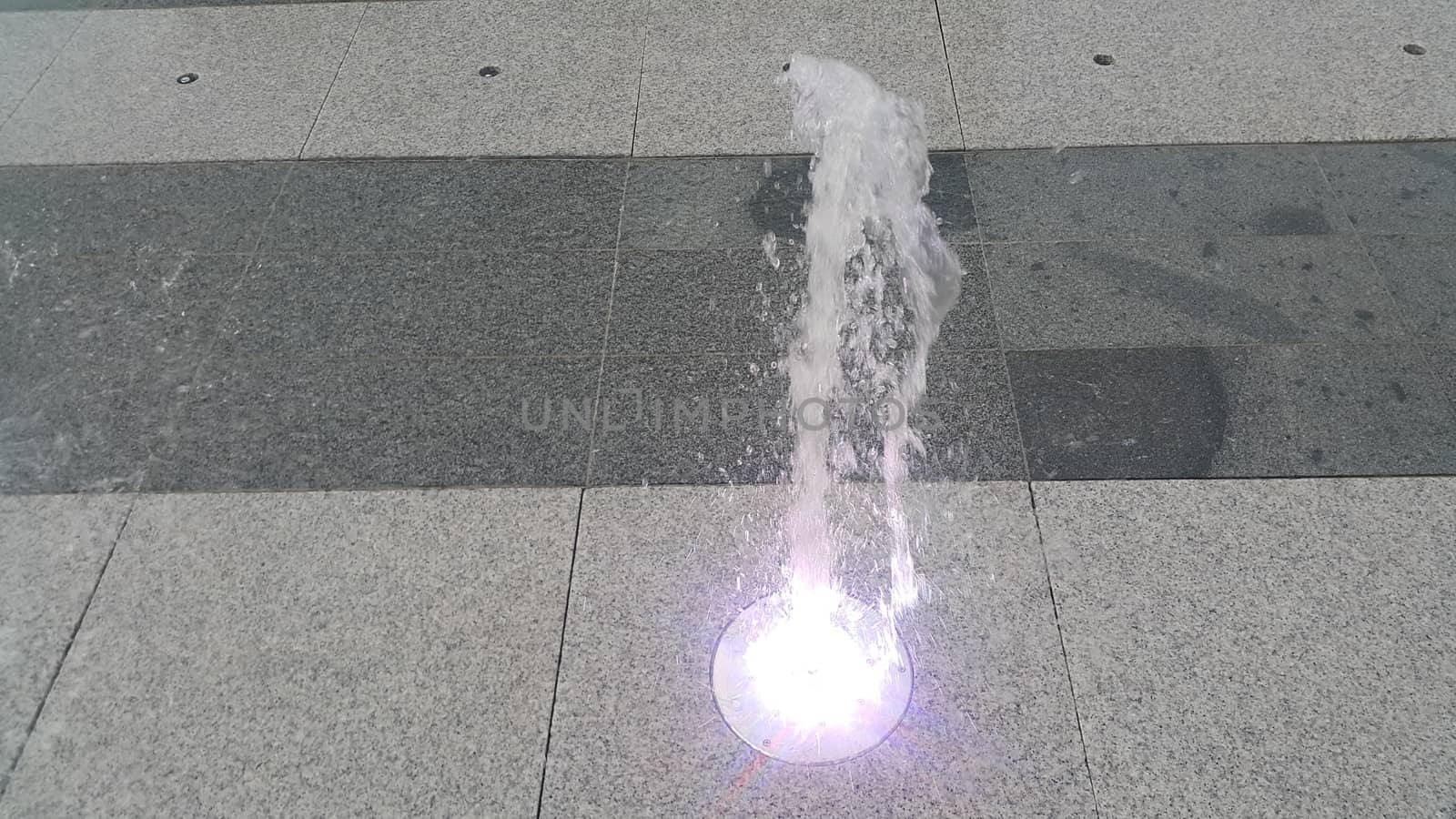 Beautiful and colorful light water fountain over concrete floor by Photochowk