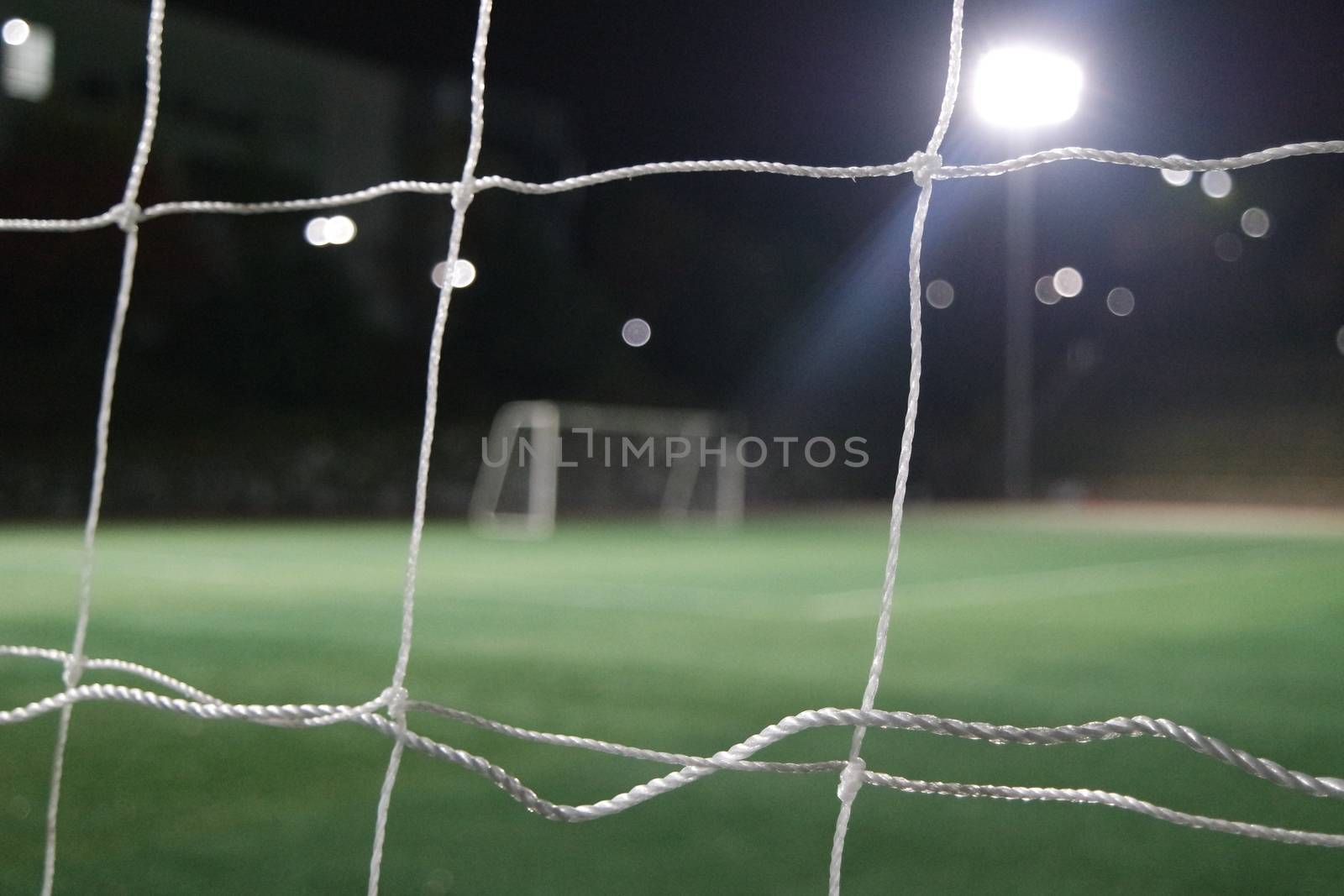 Night view of a soccer goal net under flood lights. Closeup view of goal net in a soccer playground