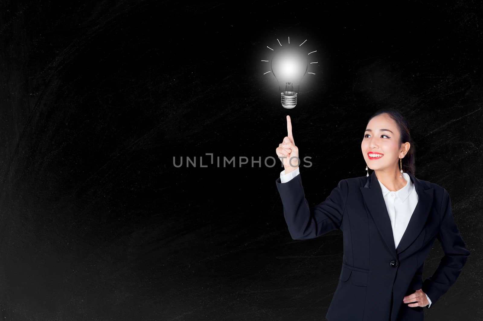 Happy young business woman pointing light bulb with inspiration and idea concept to blackboard background