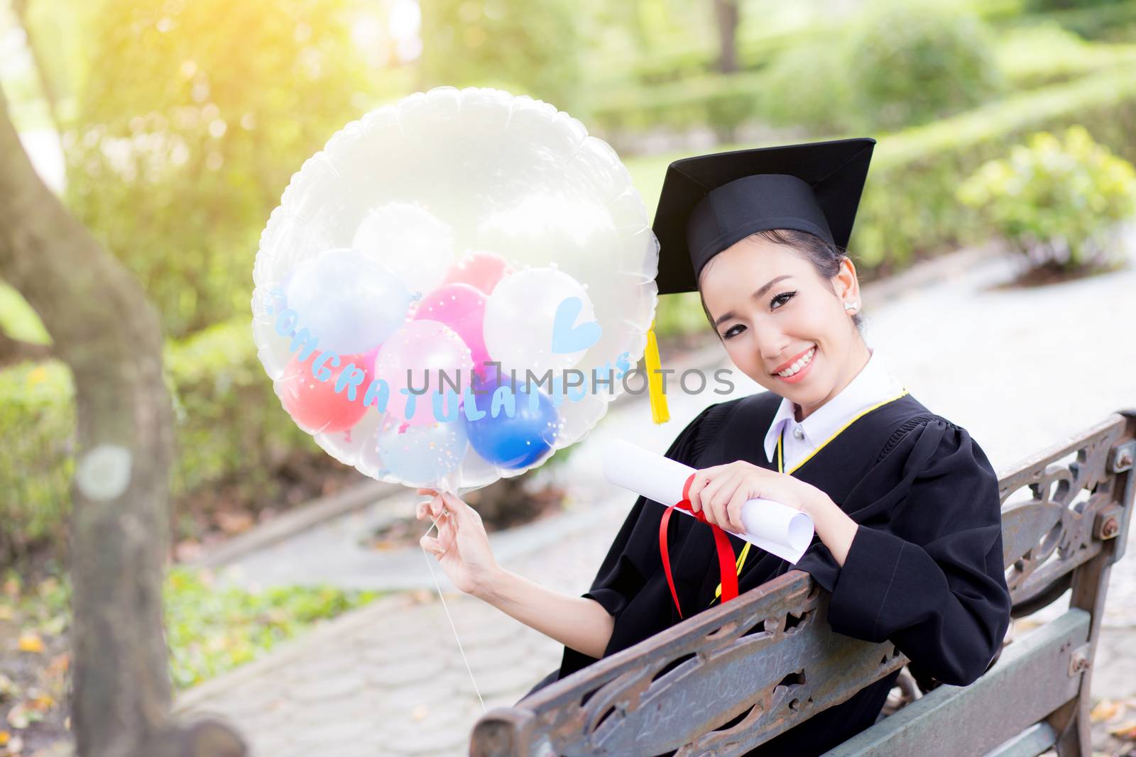 Portrait of happy young female graduates in academic dress and square academic cap holding word quotes of CONGRATS GRAD on balloon after convocation ceremony.