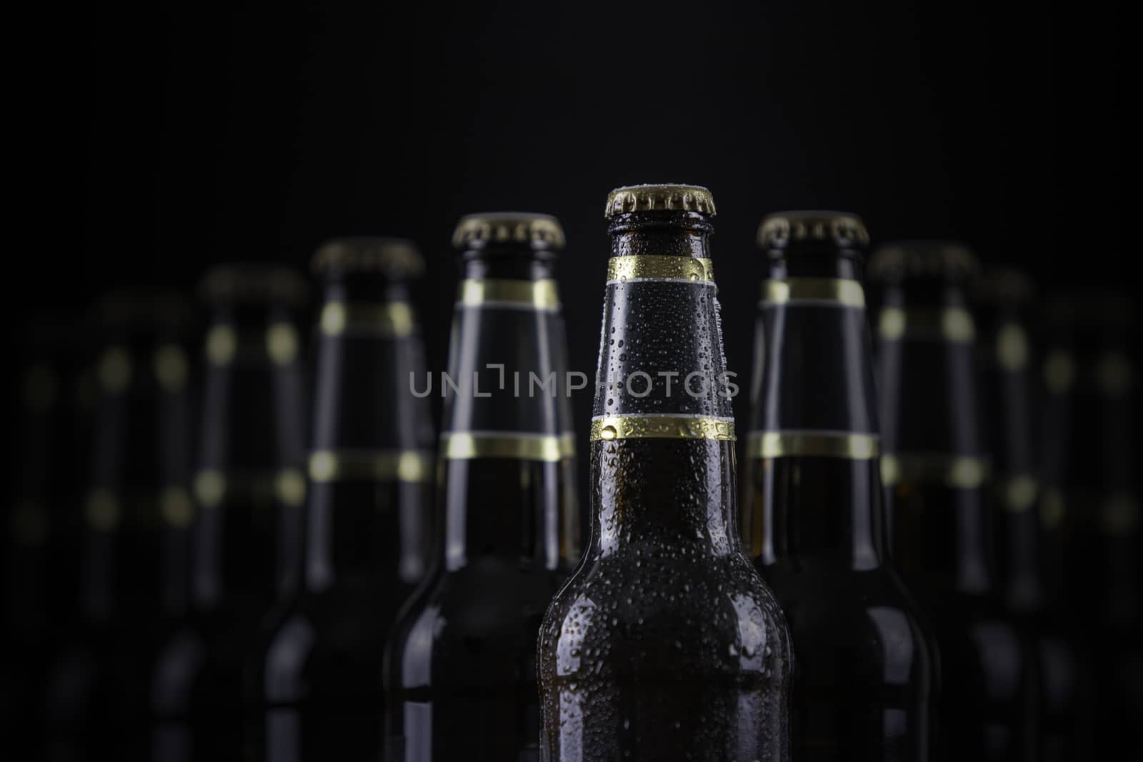 Beer bottles with blank labels lined up in selective focus on black background, one with frost droplets