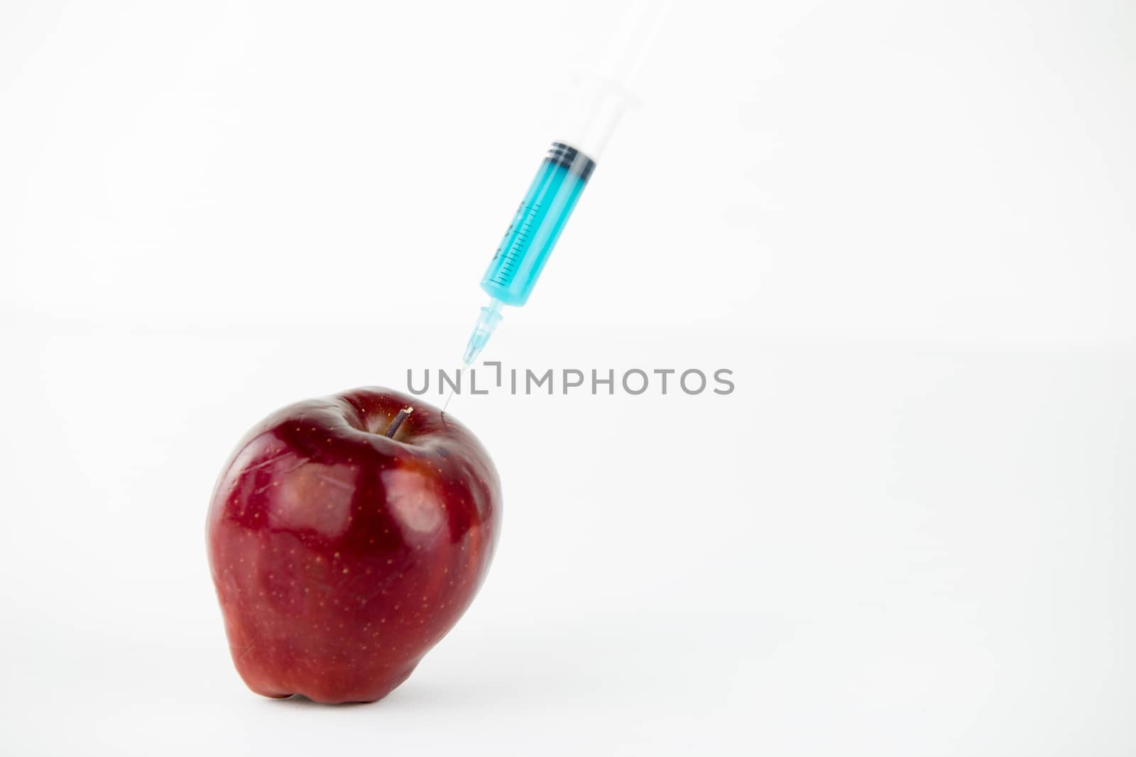 Concept: human GMO manipulation of nature and relative poisoned fruits. Close-up of an apple contaminated with a syringe threaded in and white background by robbyfontanesi