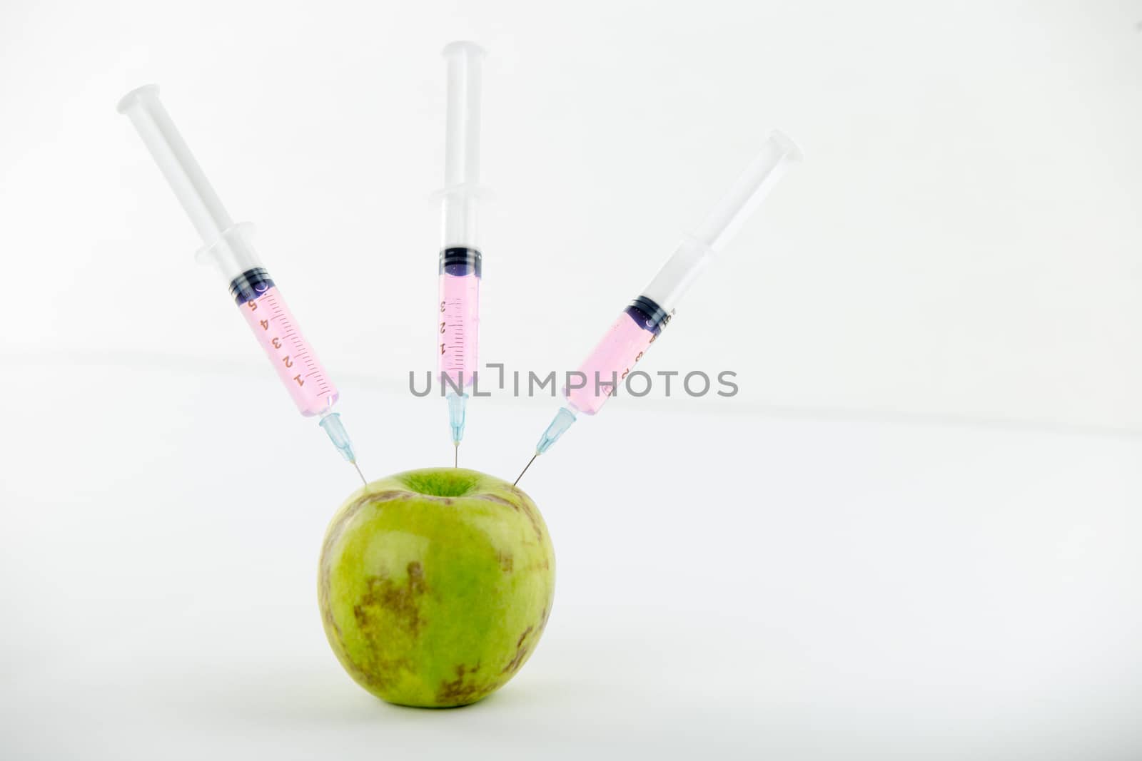 Concept: human GMO manipulation of nature and relative poisoned fruits. Close-up of an apple contaminated with three syringes threaded in and white background