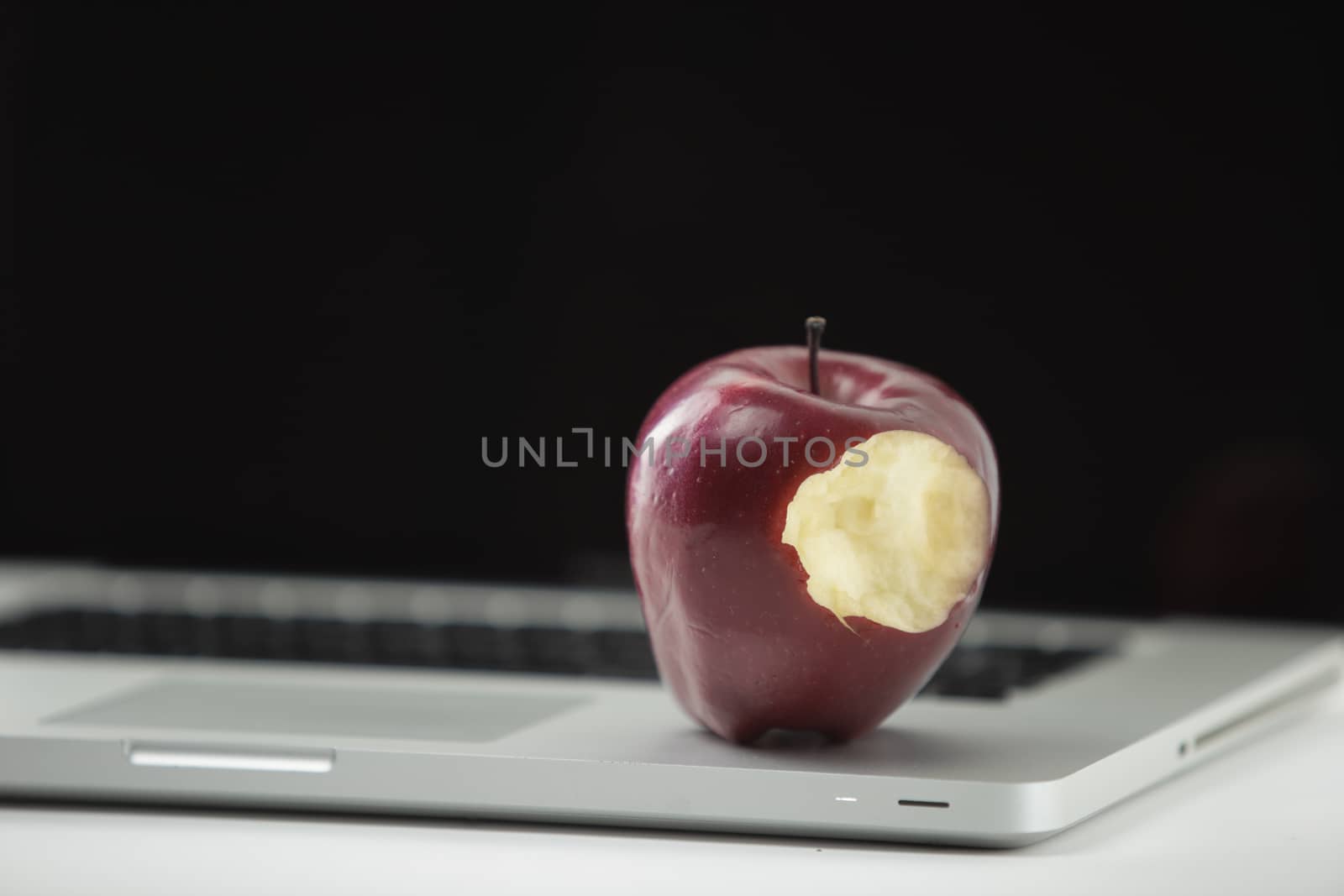 Shiny red apple resting on an open aluminum laptop in selective focus on white background by robbyfontanesi