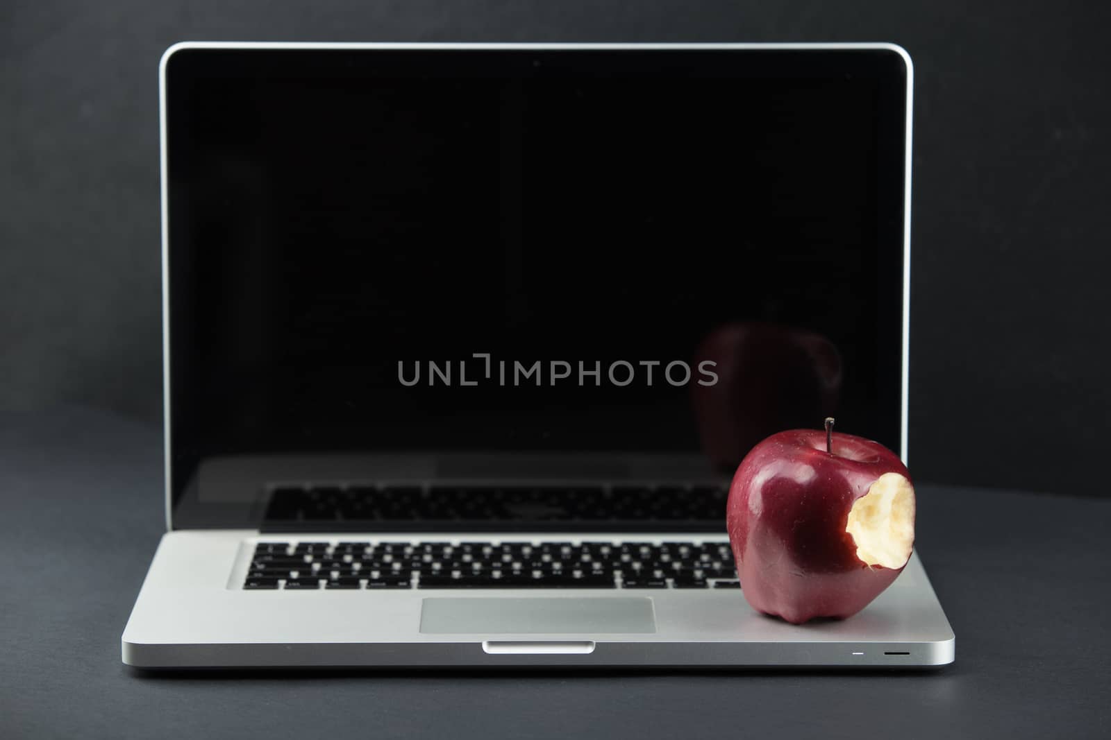 Shiny red apple resting on an open aluminum laptop in selective focus on a black background by robbyfontanesi