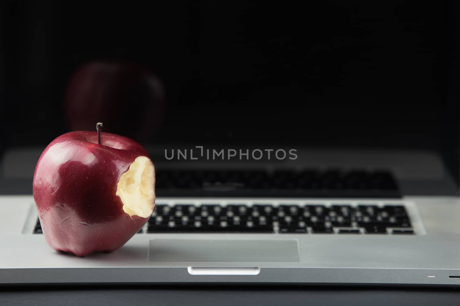 Shiny red apple resting on an open aluminum laptop in selective focus on a black background