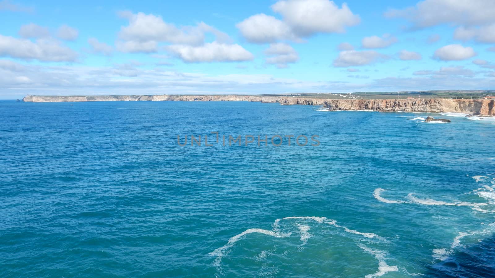 Panoramic view of the ocean cliffs of the Algarve, Portugal, with cloudy blue sky by robbyfontanesi