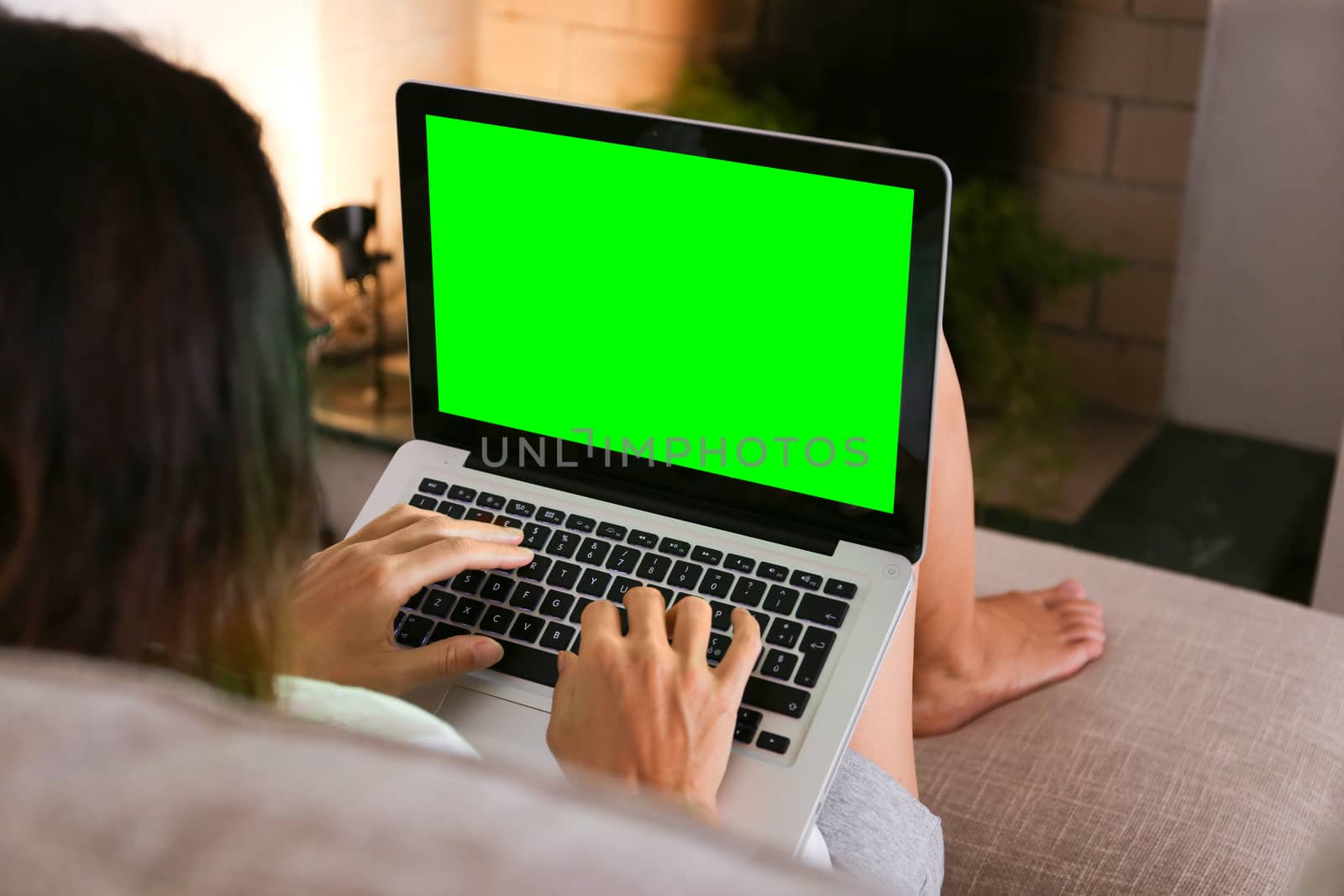 A young woman works on her laptop with the green screen at home sitting on the sofa in her living room