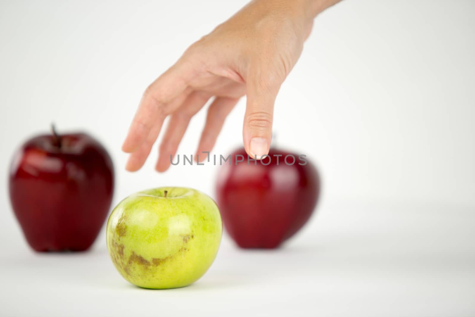 Concept of diversity: a woman's hand is about to grab the only green apple among the other red ones