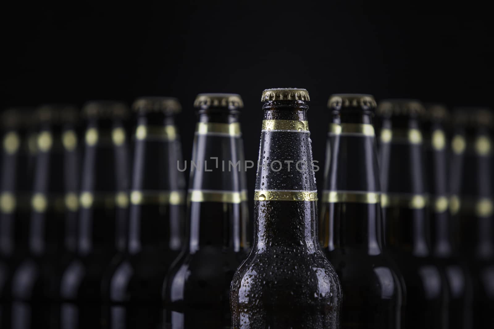 Beer bottles with blank labels lined up in selective focus on black background, one with frost droplets