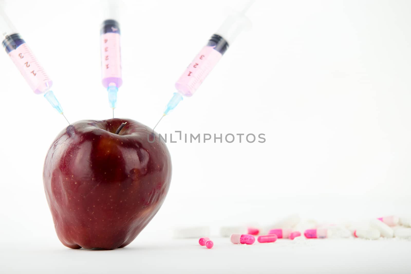 Concept: human GMO manipulation of nature and relative poisoned fruits. Close-up of an apple contaminated with three syringe threaded in and medicines on a white background by robbyfontanesi