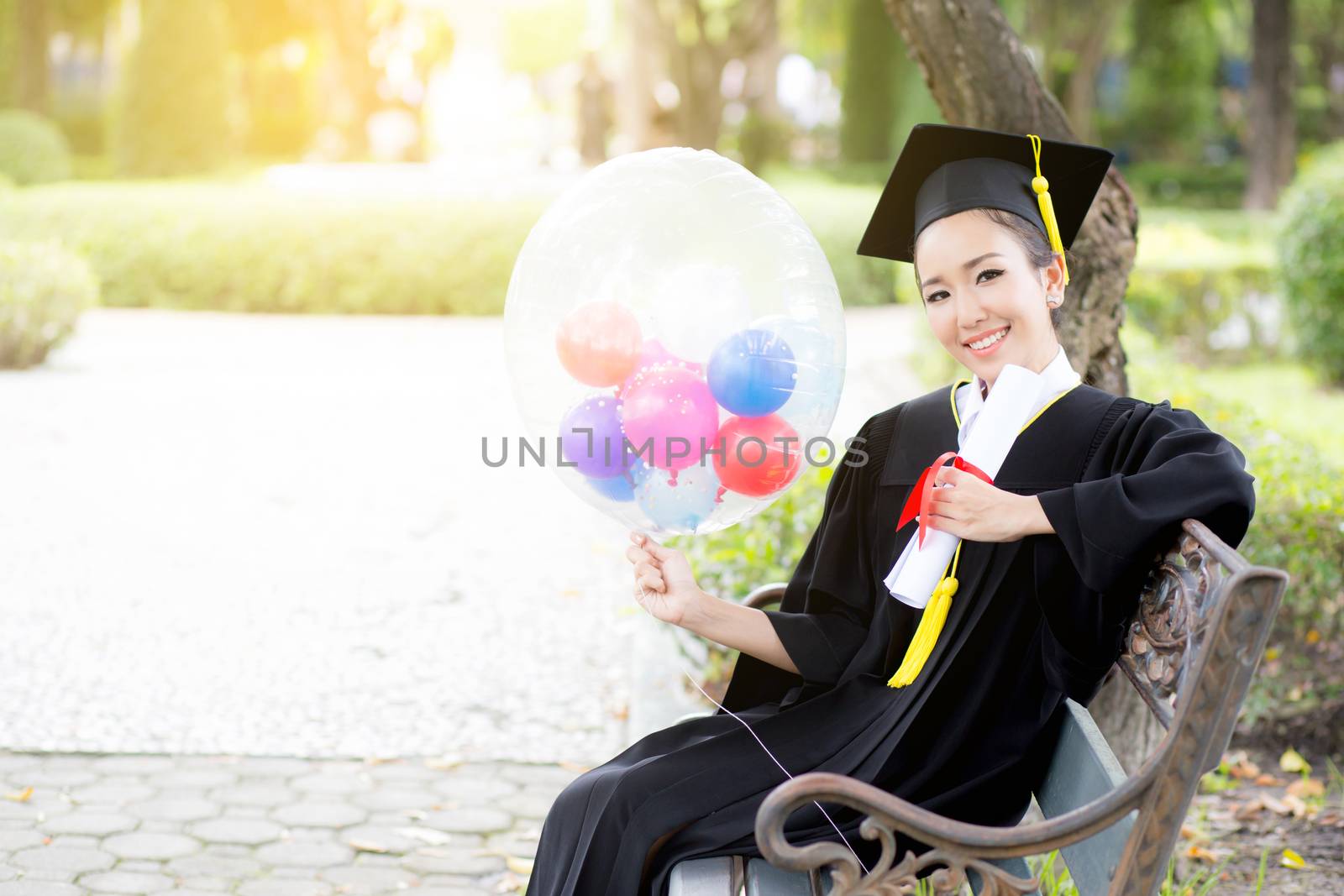 Portrait of happy young female graduates in academic dress and square academic cap holding word quotes of CONGRATS GRAD on balloon after convocation ceremony.