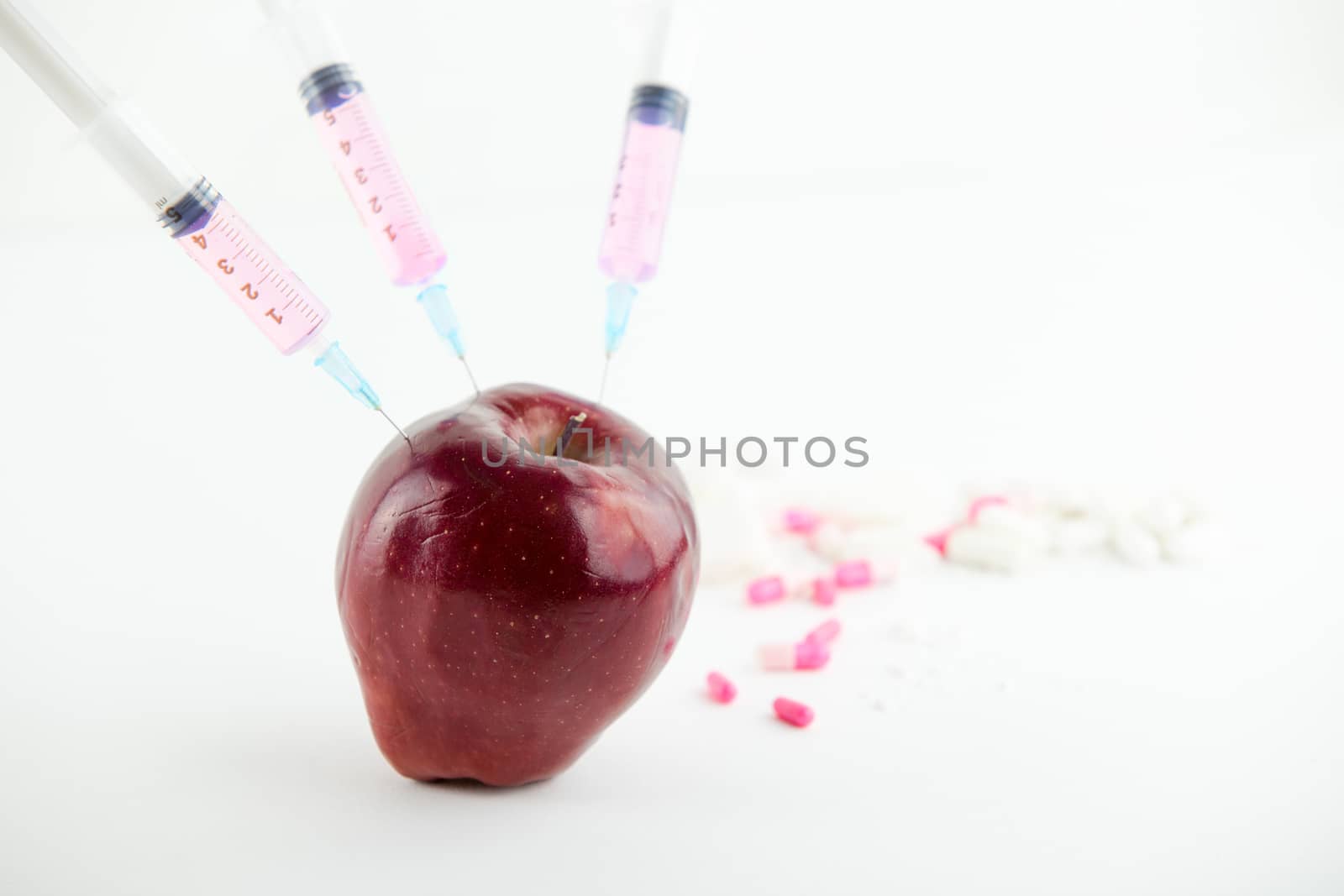 Concept: human GMO manipulation of nature and relative poisoned fruits. Close-up of an apple contaminated with three syringe threaded in and medicines on a white background by robbyfontanesi