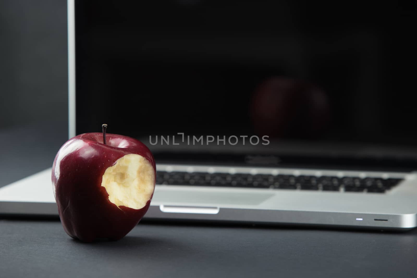 Shiny red apple resting on an open aluminum laptop in selective focus on a black background