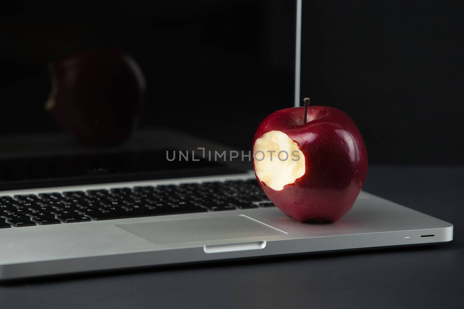 Shiny red apple resting on an open aluminum laptop in selective focus on a black background by robbyfontanesi