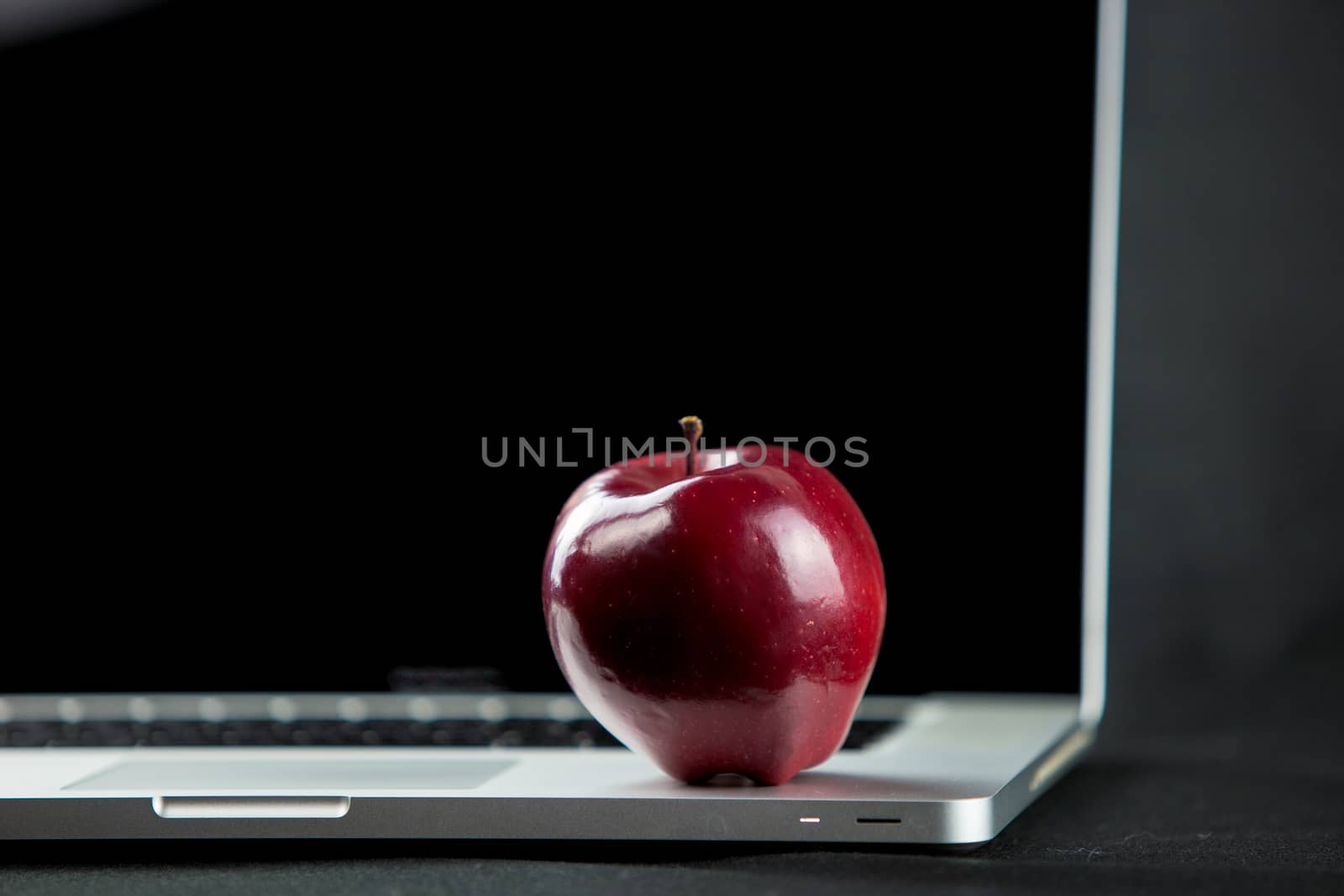 Shiny red apple resting on an open aluminum laptop in selective focus on a black background by robbyfontanesi