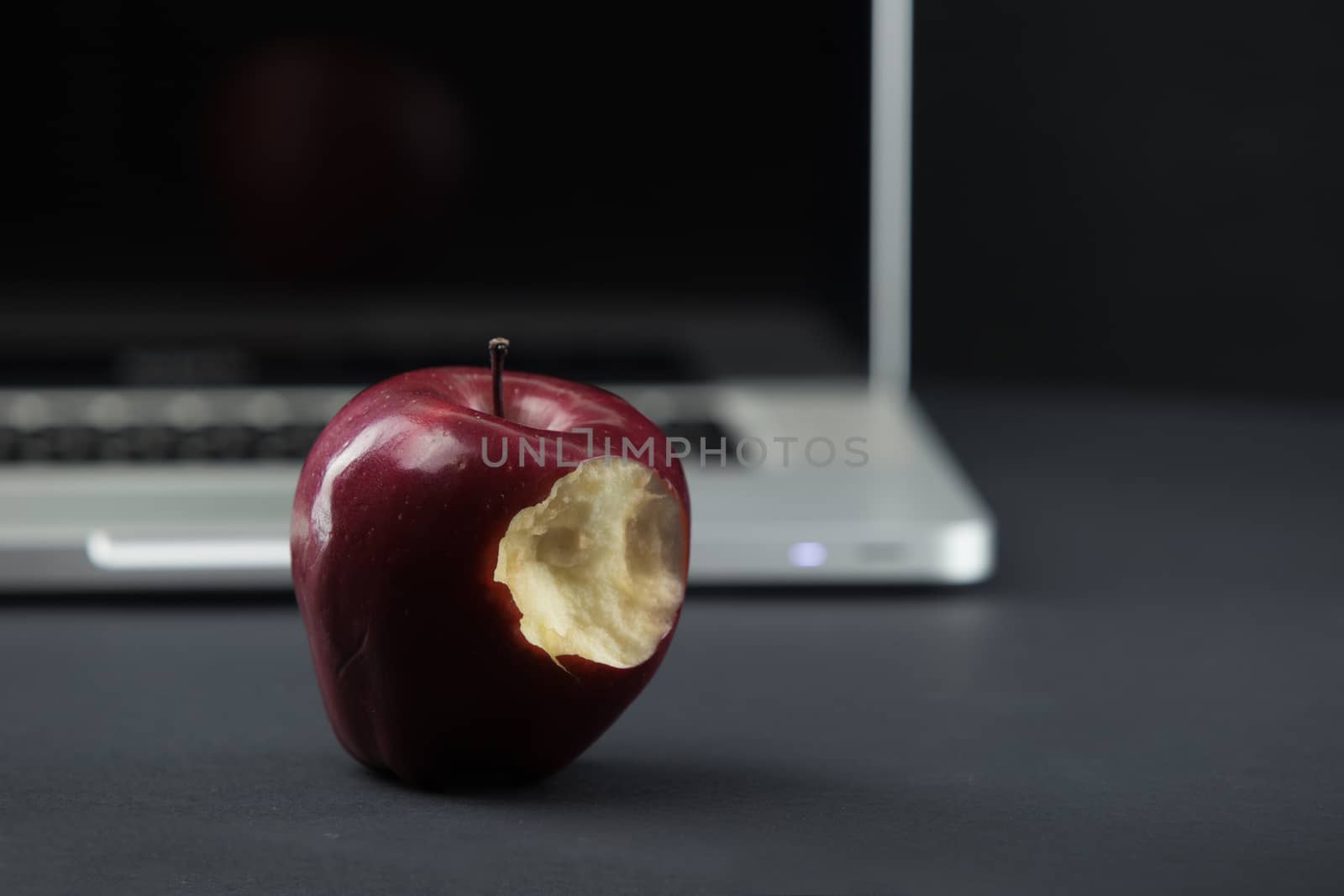 Shiny red apple resting on an open aluminum laptop in selective focus on a black background by robbyfontanesi