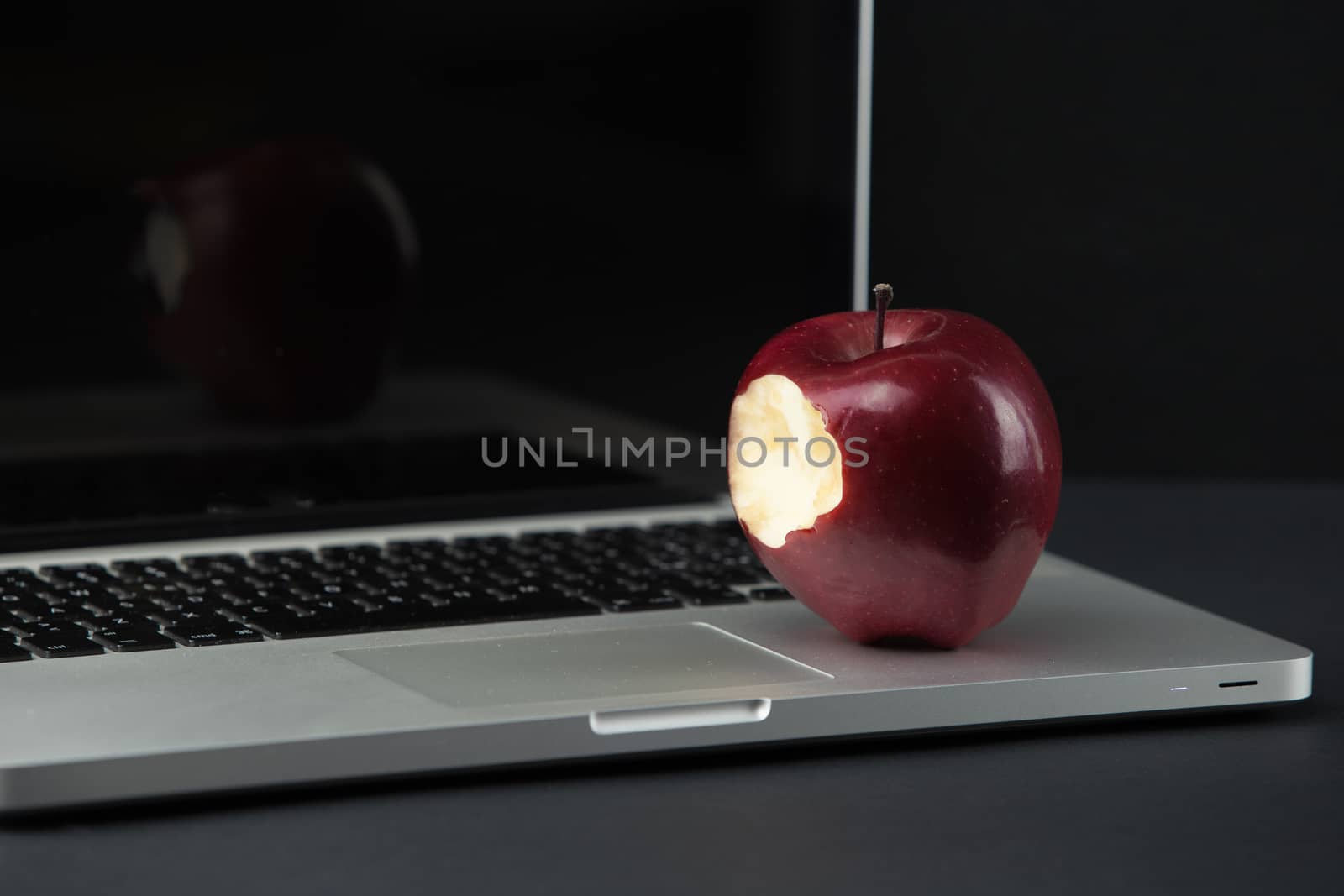 Shiny red apple resting on an open aluminum laptop in selective focus on a black background by robbyfontanesi