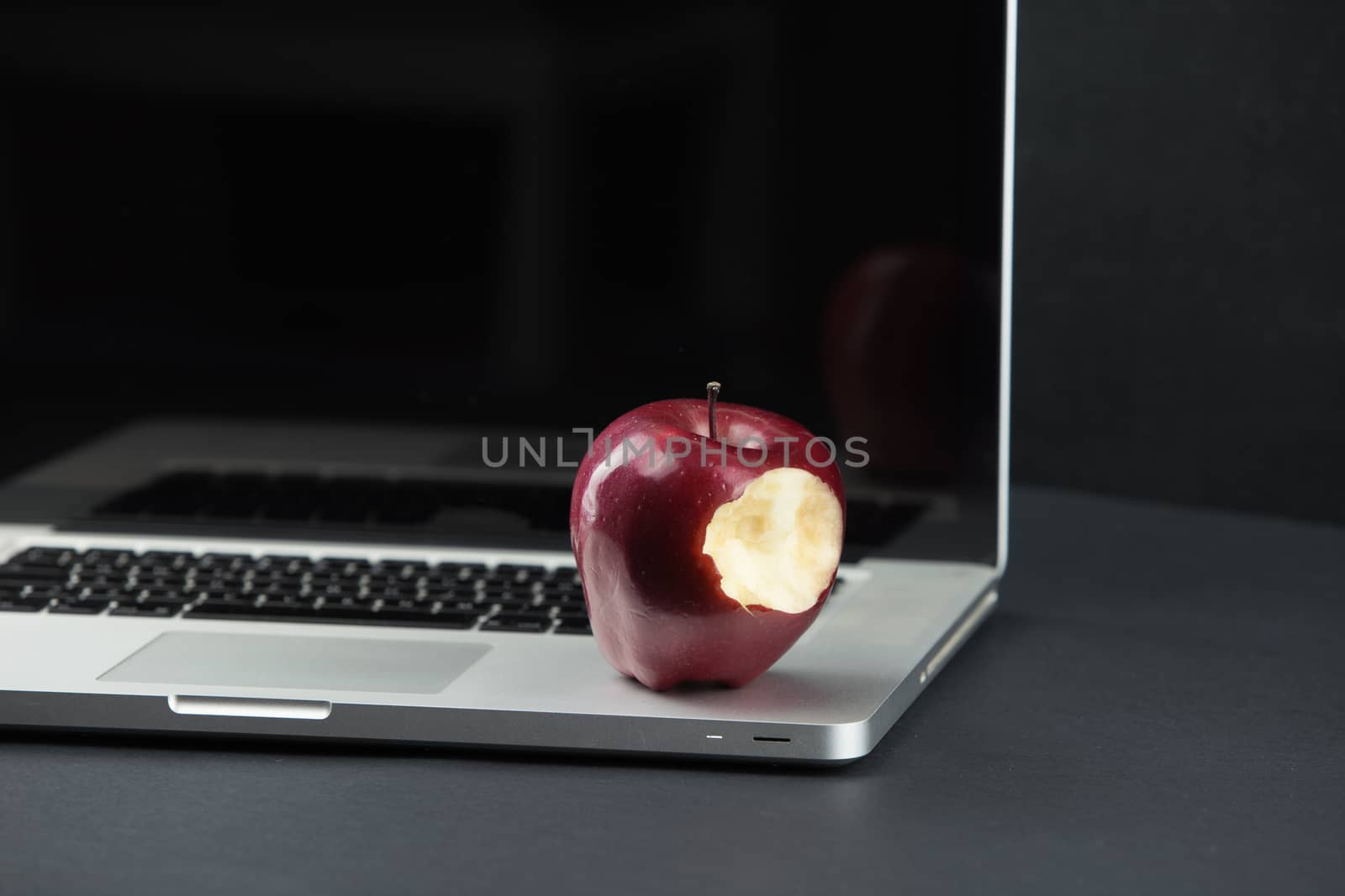 Shiny red apple resting on an open aluminum laptop in selective focus on a black background by robbyfontanesi