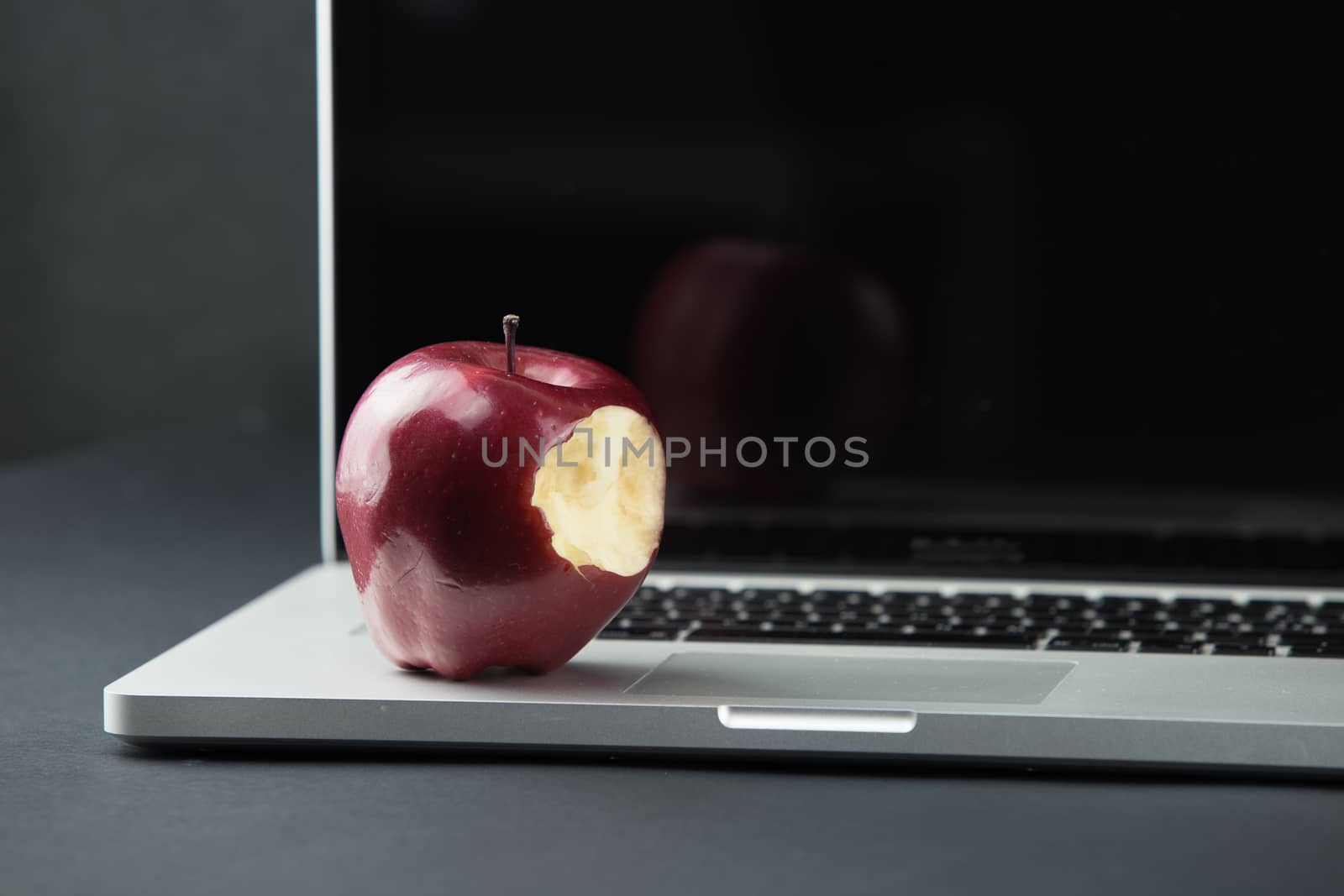 Shiny red apple resting on an open aluminum laptop in selective focus on a black background