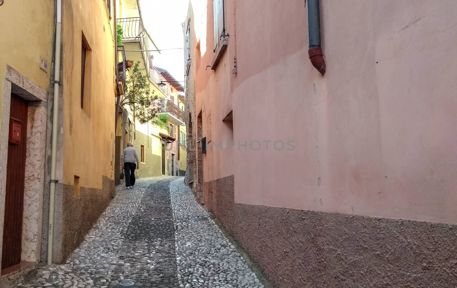 Concept: old age. An elderly man trudges along a cobblestone street in an ancient Italian village by robbyfontanesi