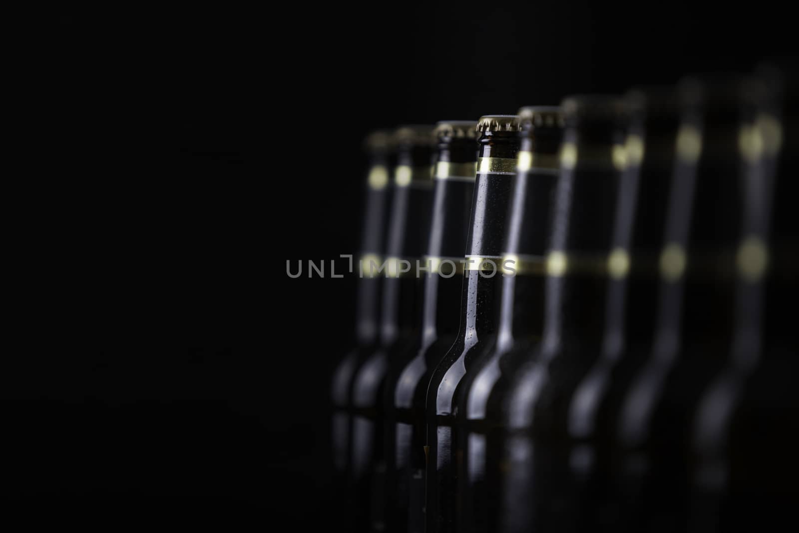 Beer bottles with blank labels lined up in selective focus on black background, one with frost droplets